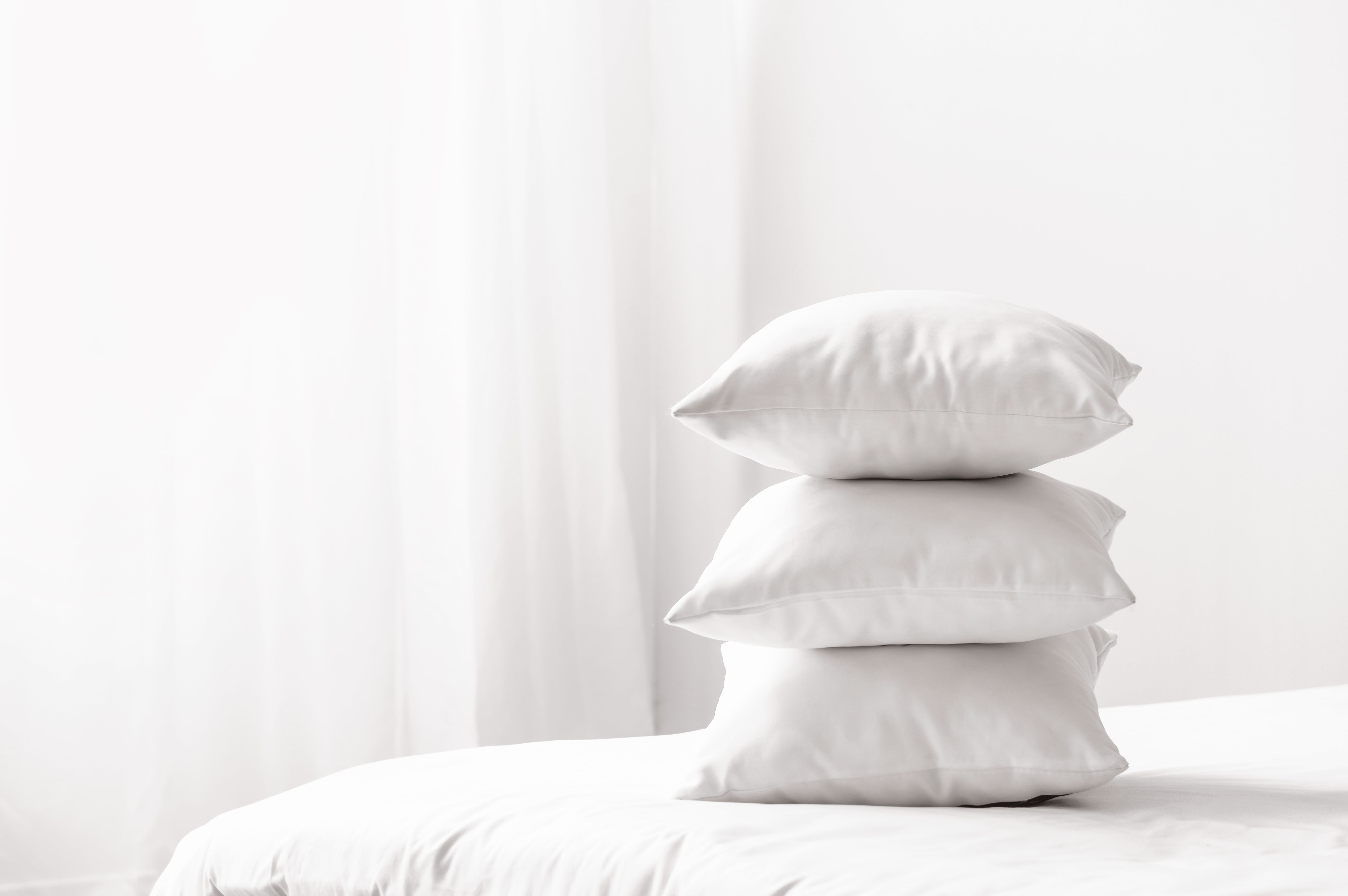 A stack of three pillows on the corner of a bed.