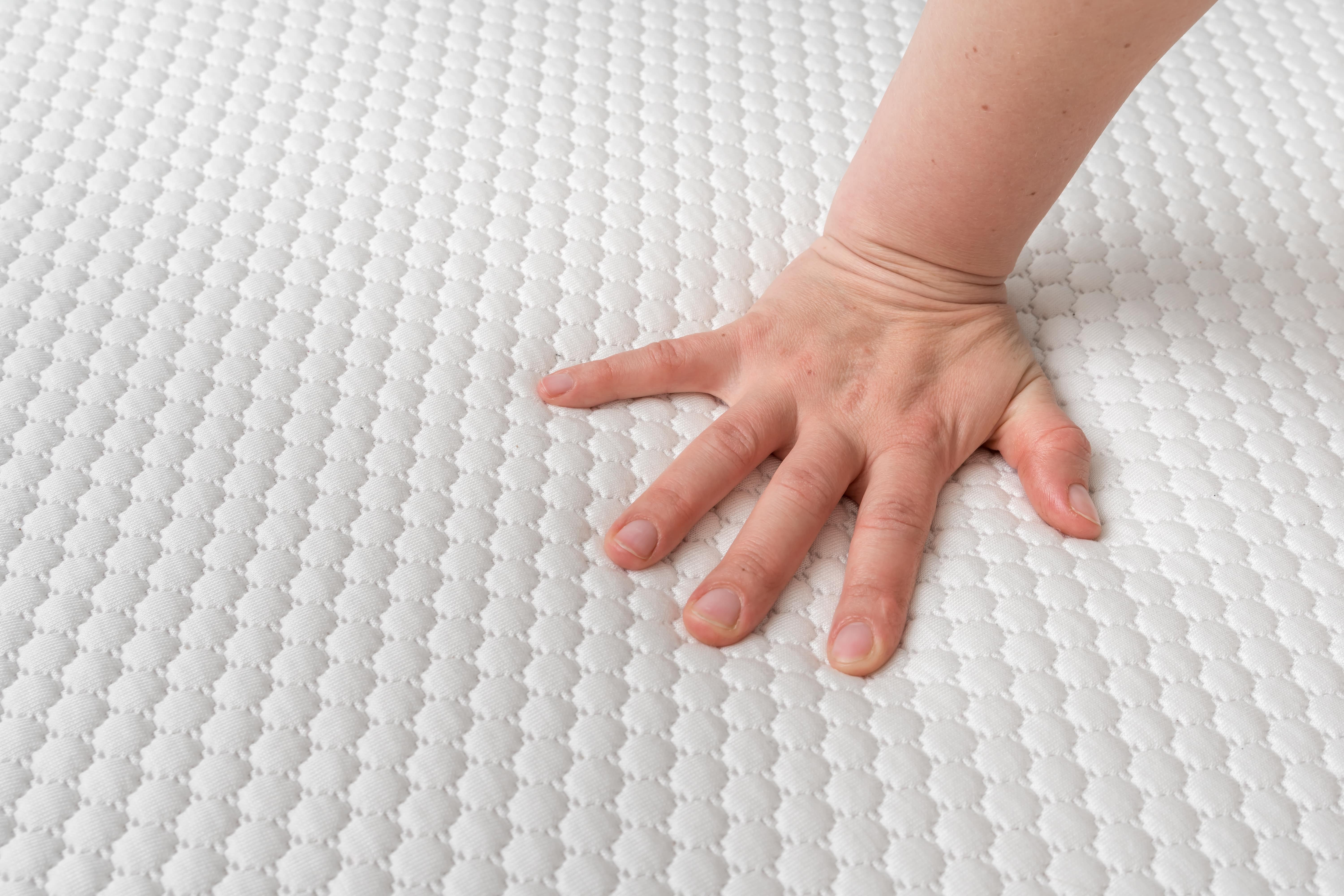 A person testing the responsiveness of the surface of their new mattress with their hand.