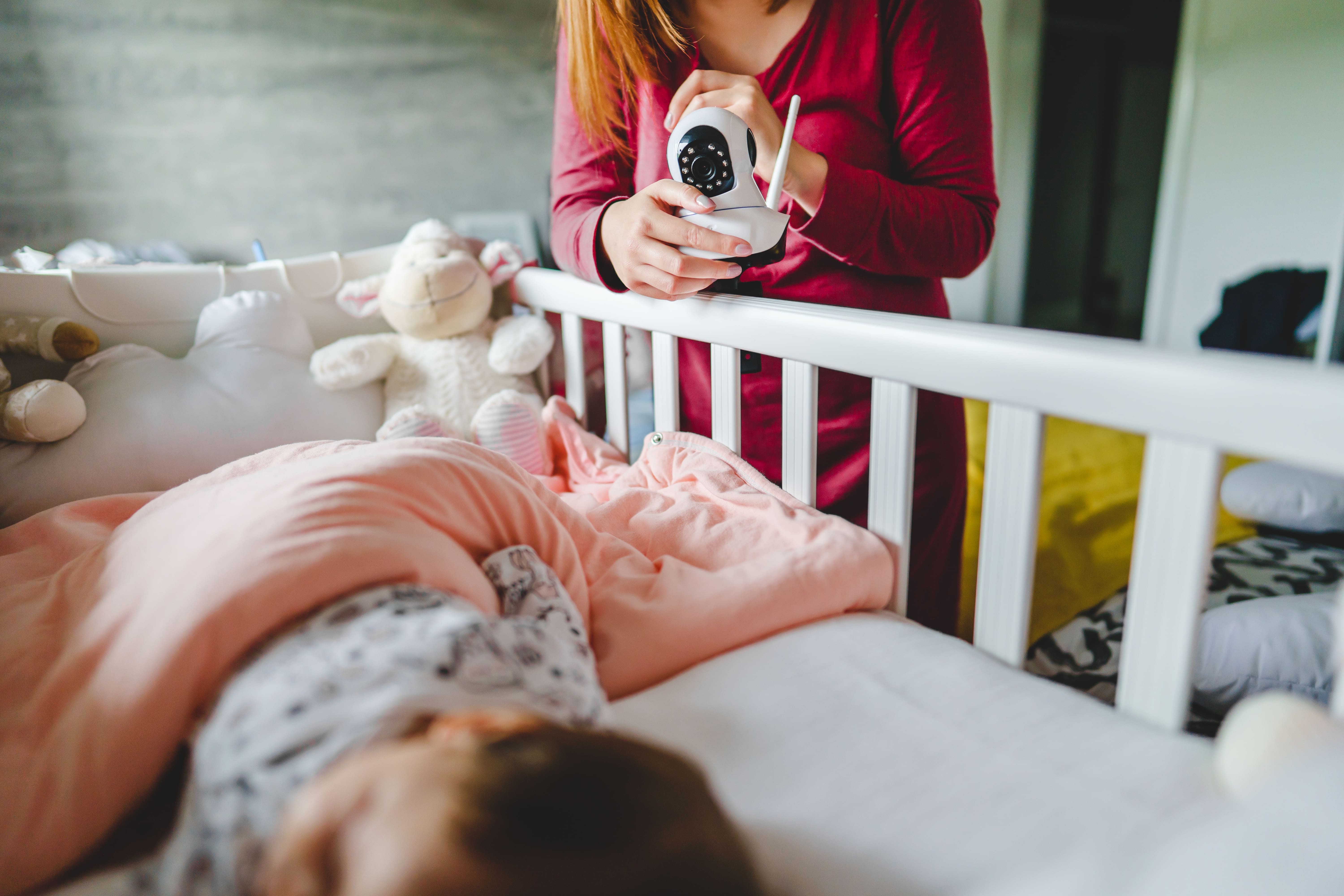 A mum setting up a baby monitoring camera as she prepares to leave the room after getting her baby off to sleep.