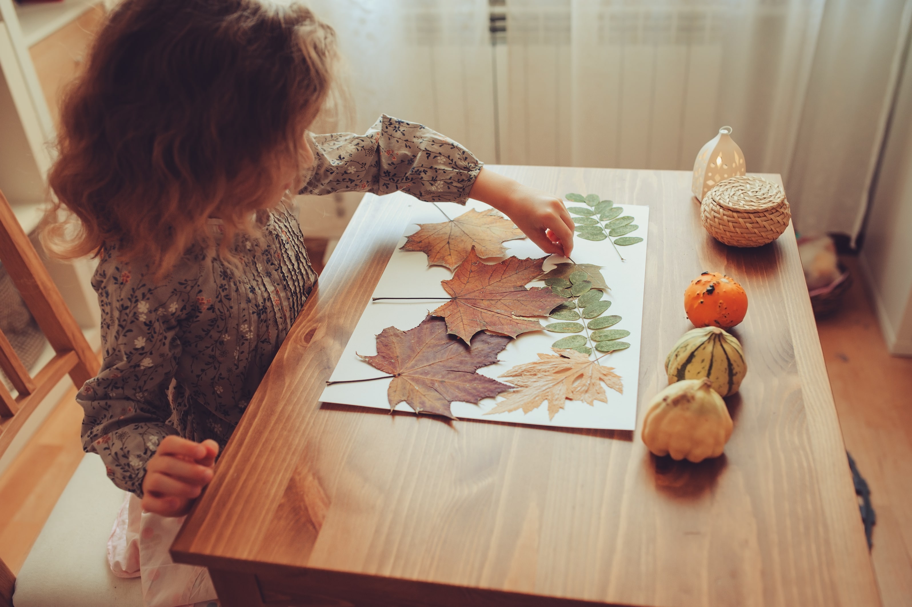 A little girl sticking autumn leaves onto a piece of plain paper to create a collage