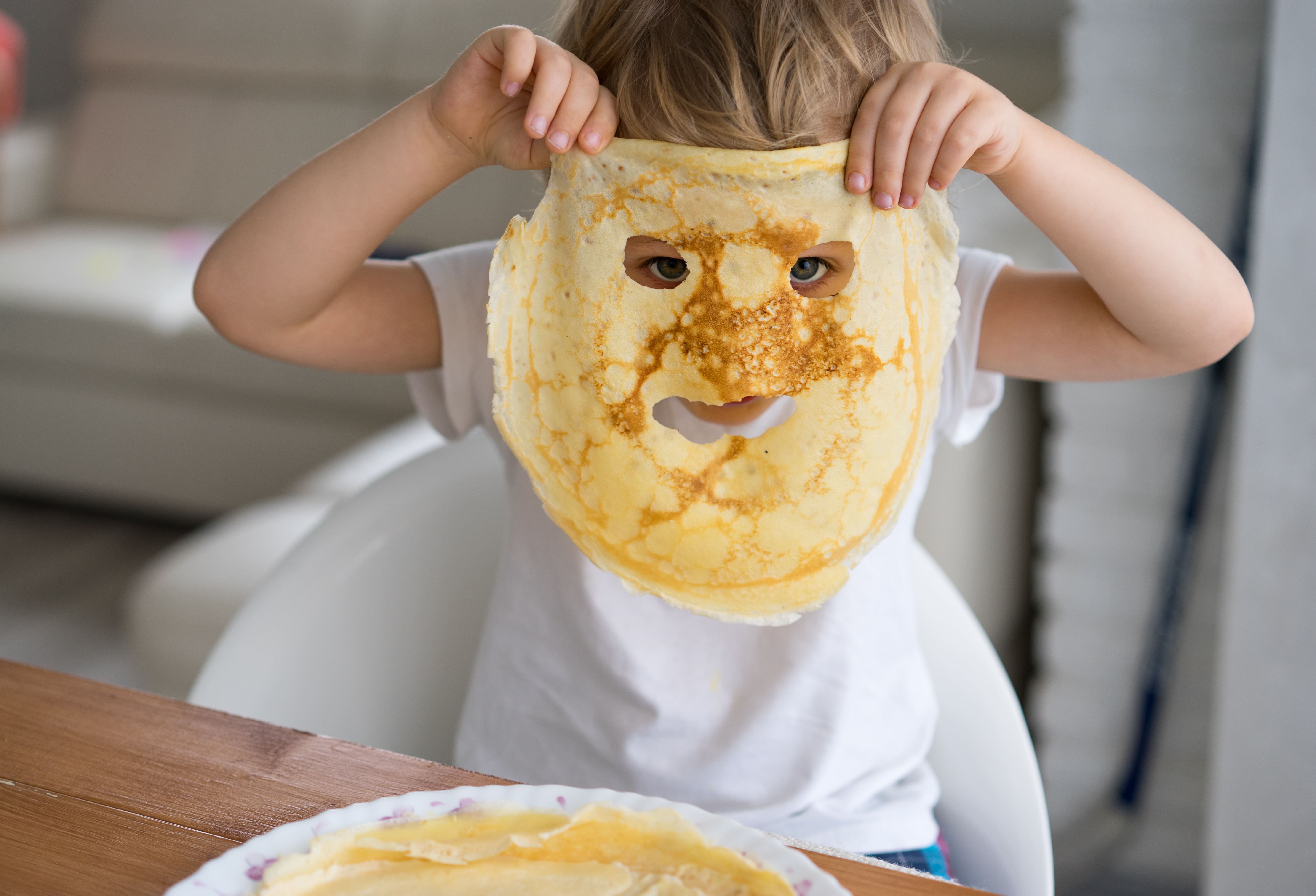 A child holding up a pancake mask to his face after eating holes in the pancake for where his eyes and mouth would need to be.