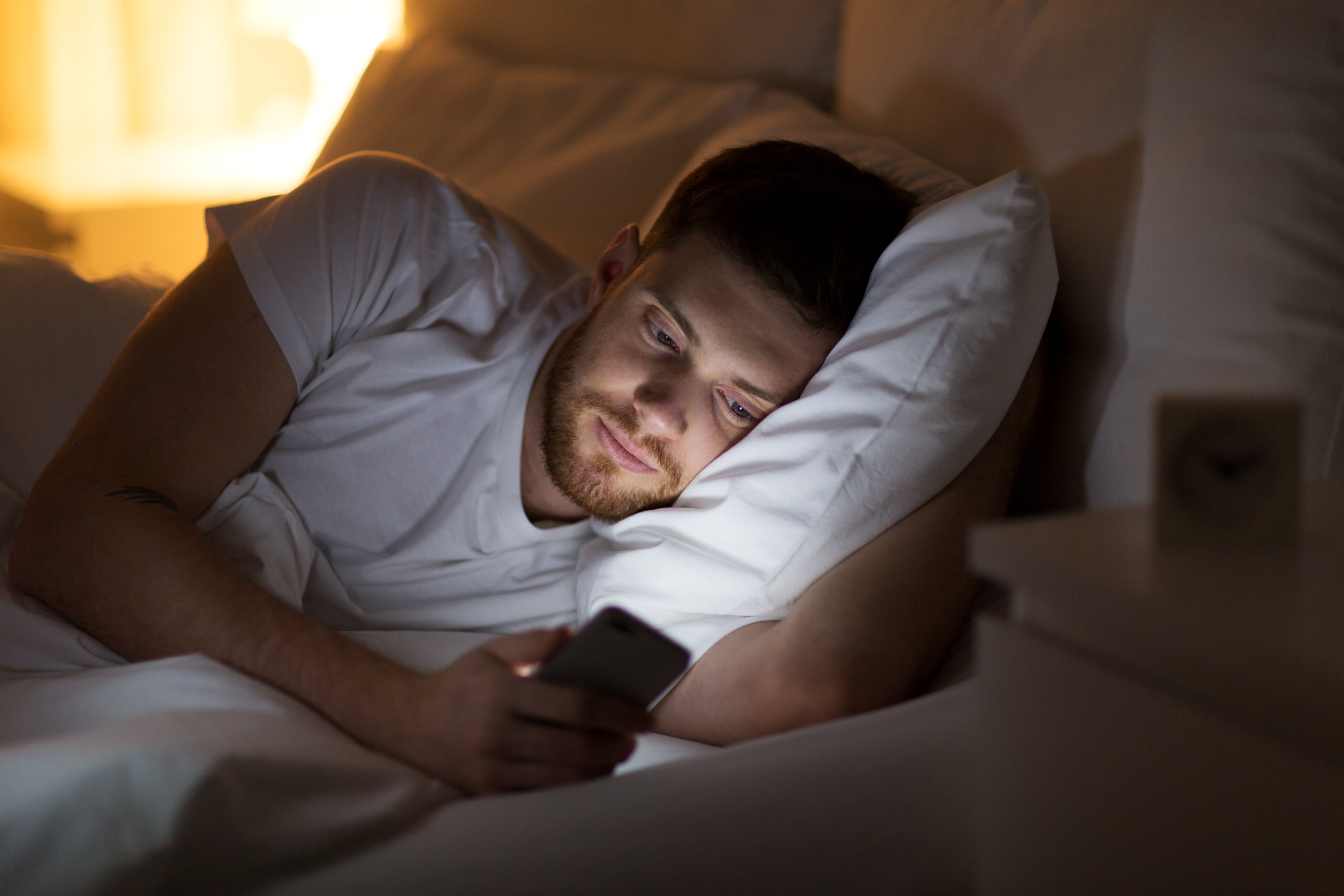 A man, lay in bed, scrolling through social media on his smartphone before going to sleep.