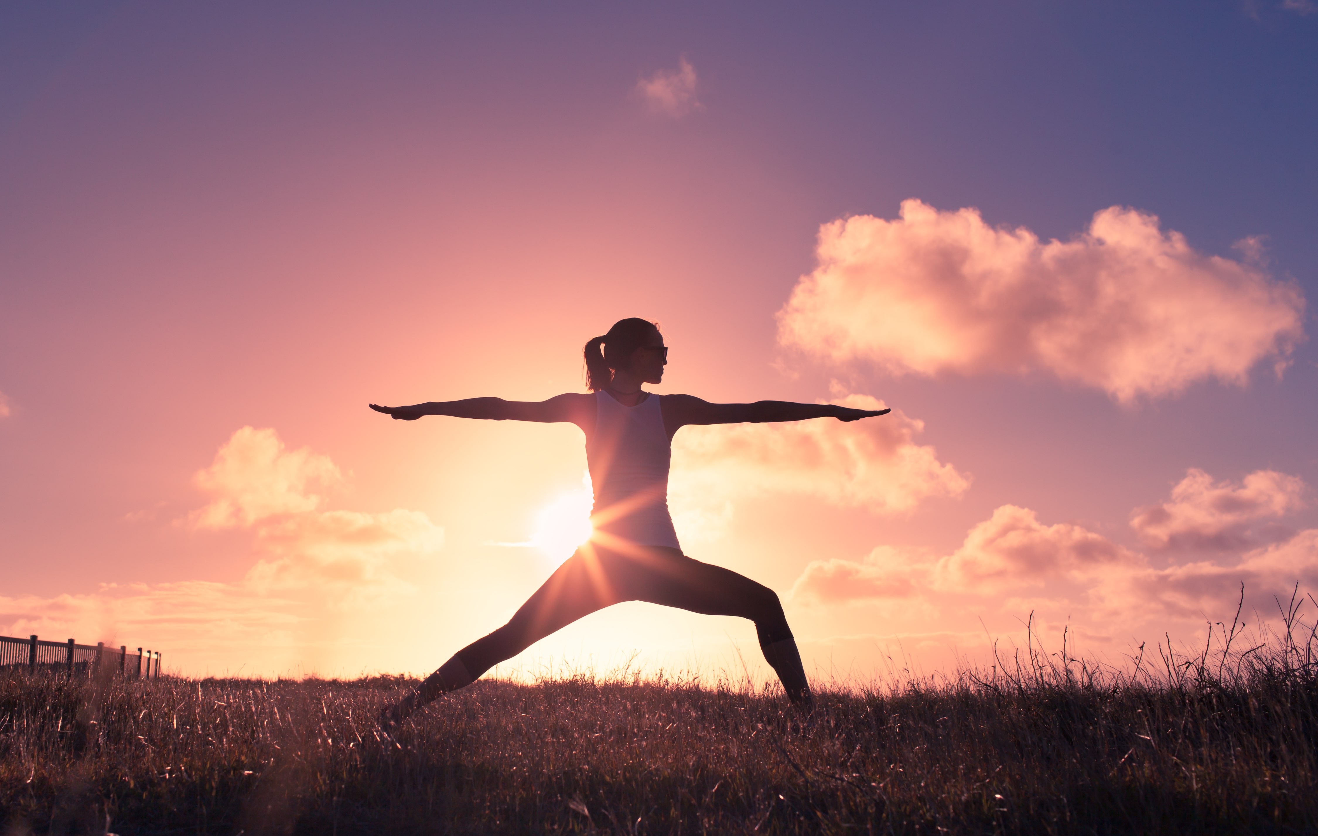 Woman in a grassy field practicing yoga as the sun glows behind her.