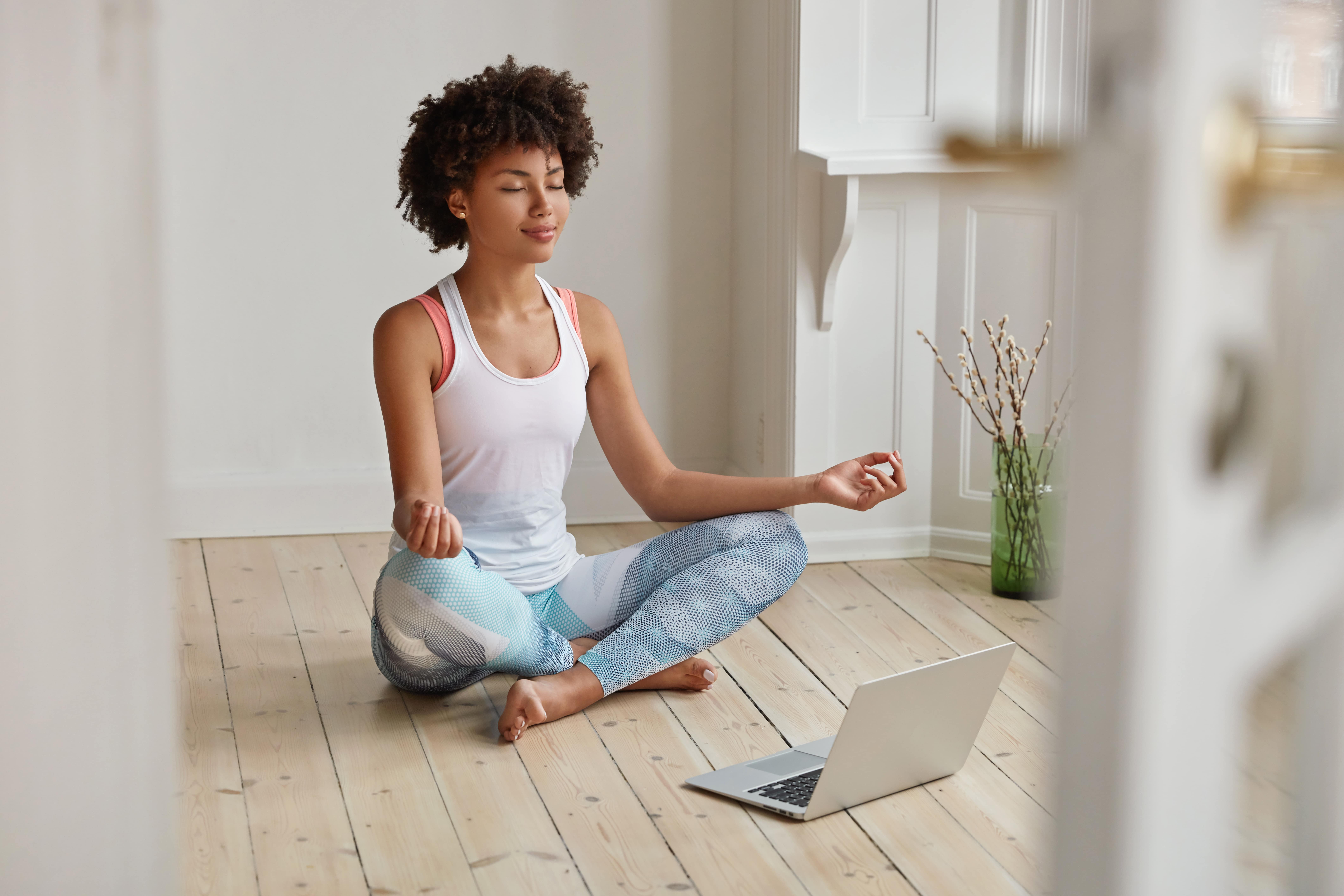 Woman sitting with legs crossed and eyes closed meditating in front of a laptop.