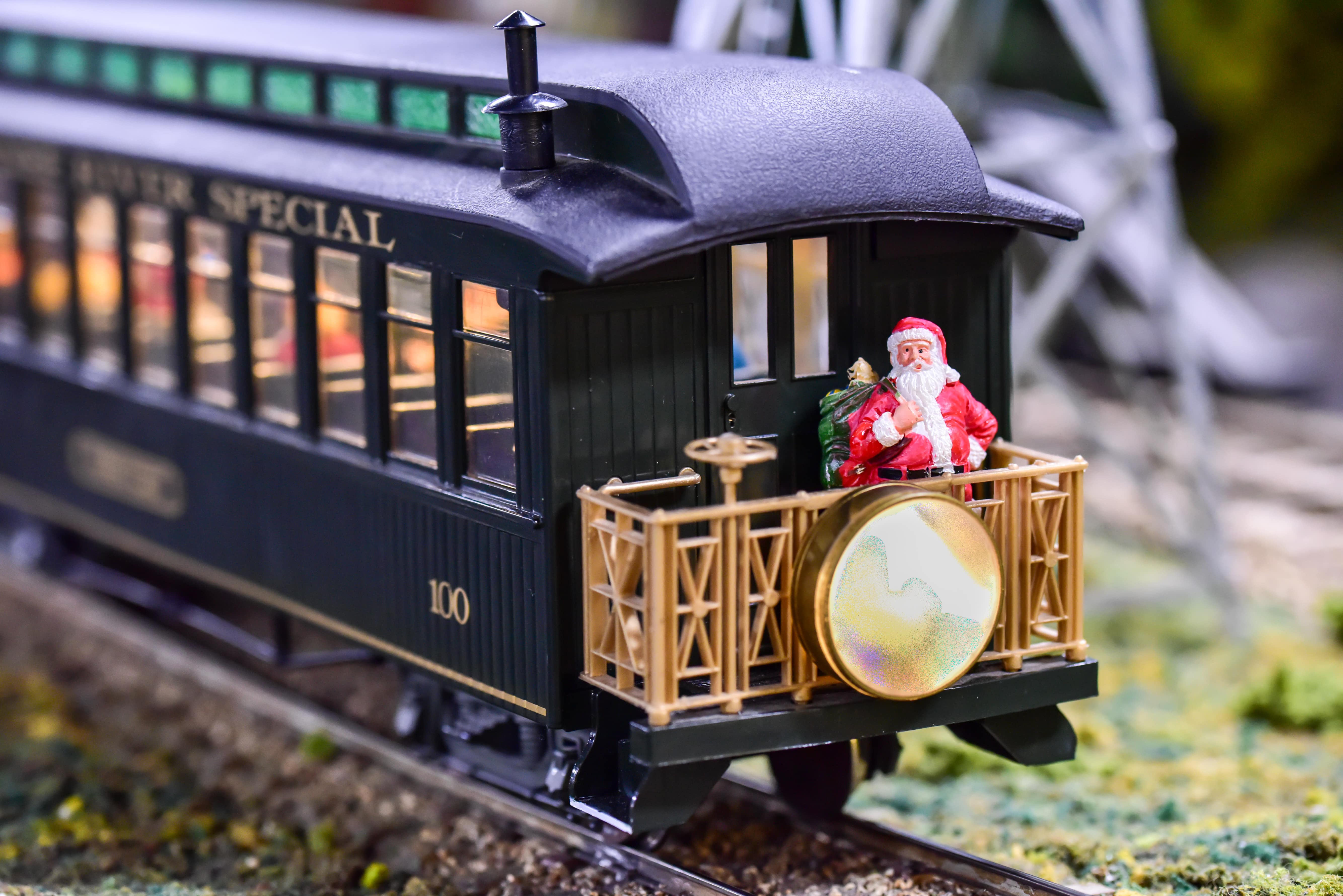 A tiny figurine of Santa holding a sack stands on at the front of a toy train on a track.