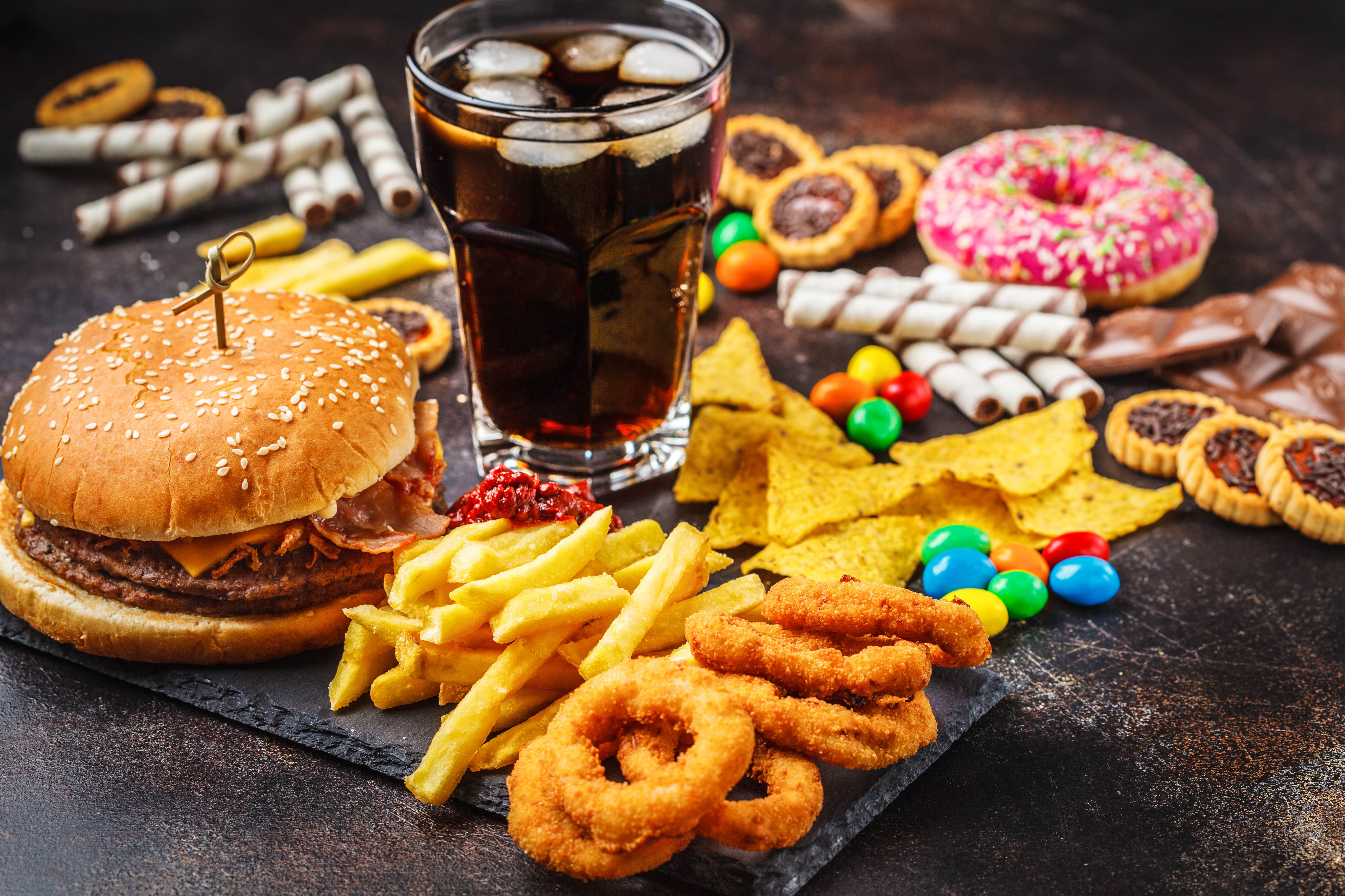 Glass of cola stands among an array of takeaway junk food, cakes and sweets