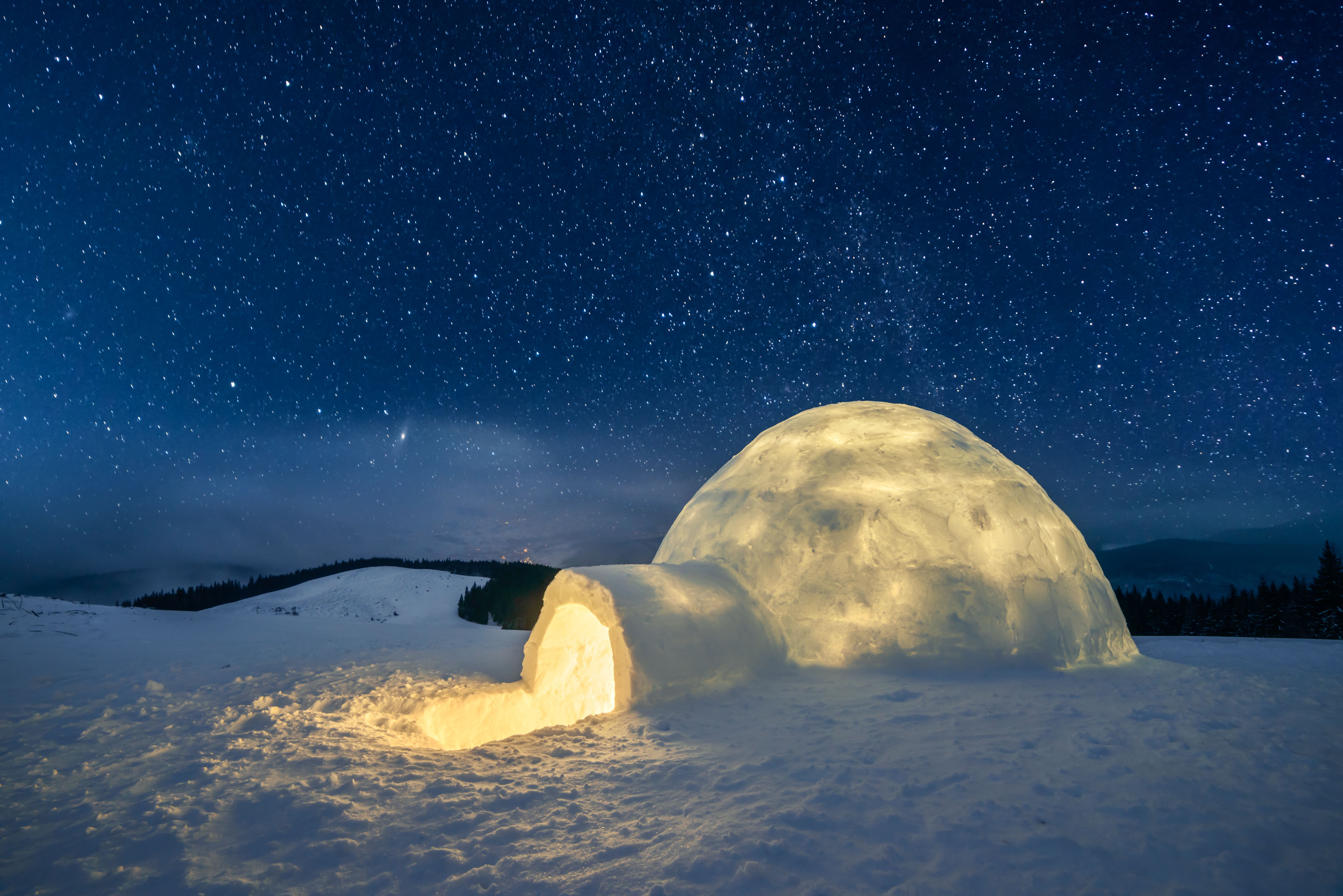 An igloo glows against a starlit backdrop and a snow-capped landscape.
