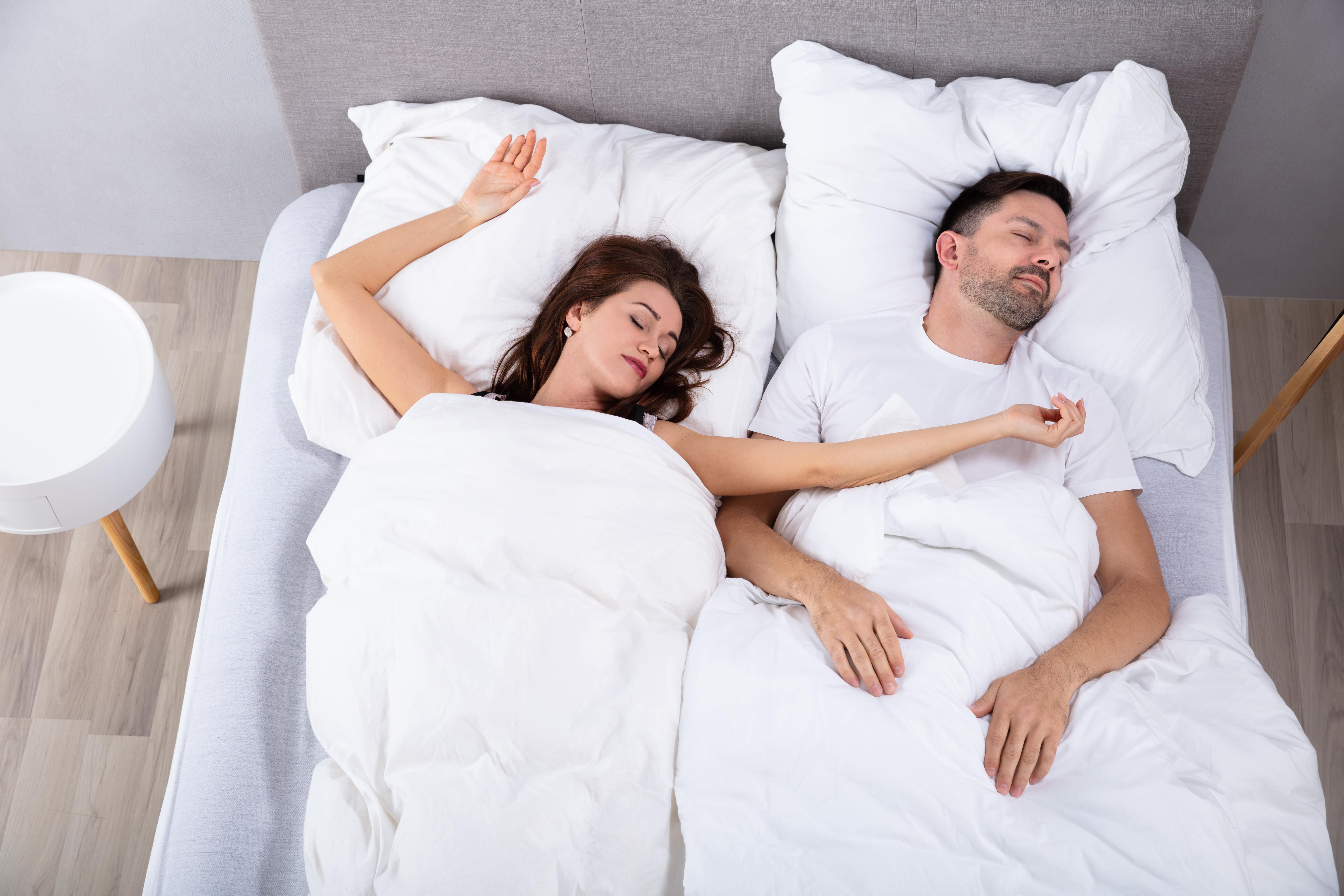 Bird's eye view of a man and woman in bed asleep. Woman has her arm flopped across the man's chest.