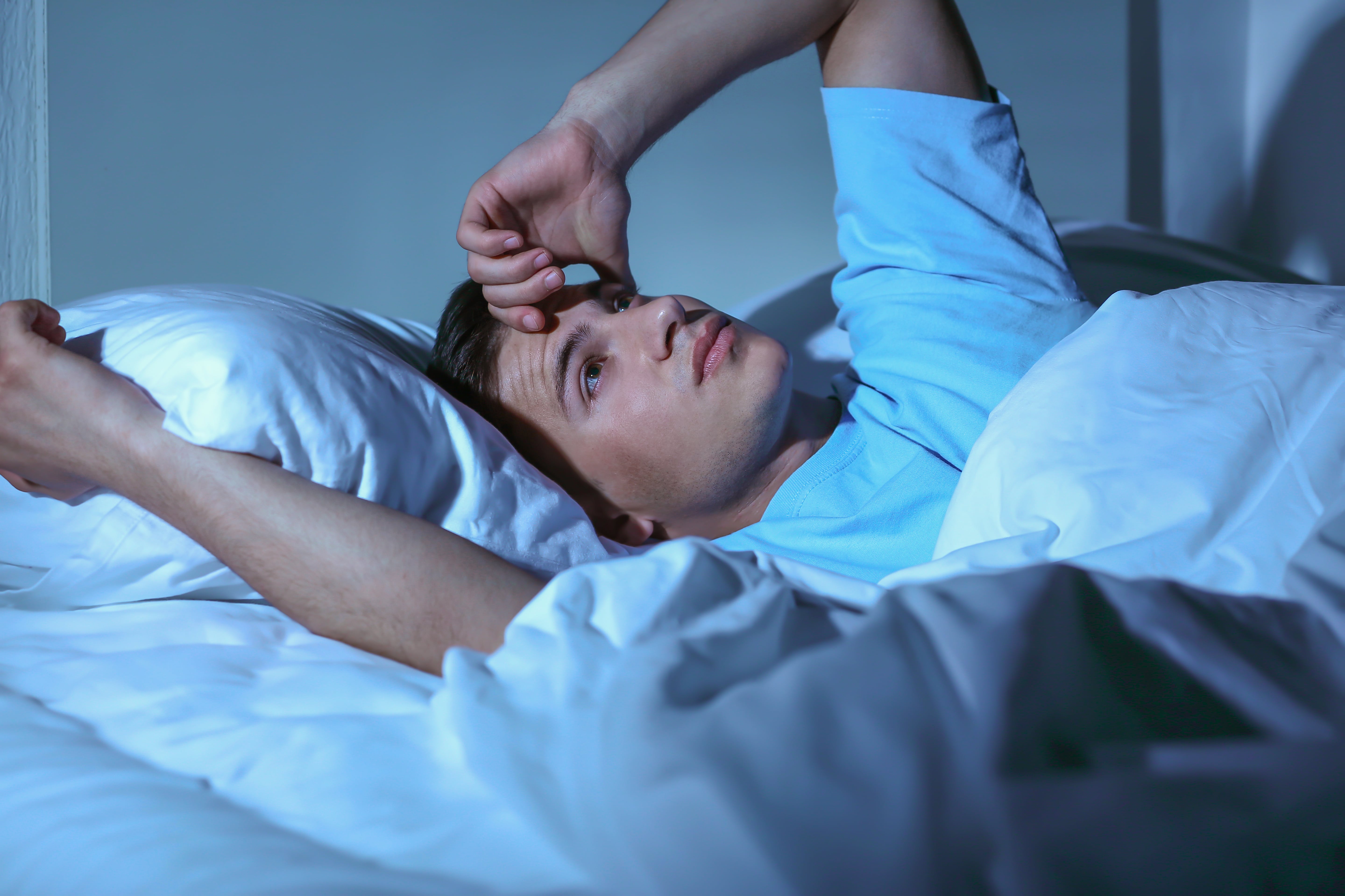 Man Lying in Bed with hand on Head Looking Stressed