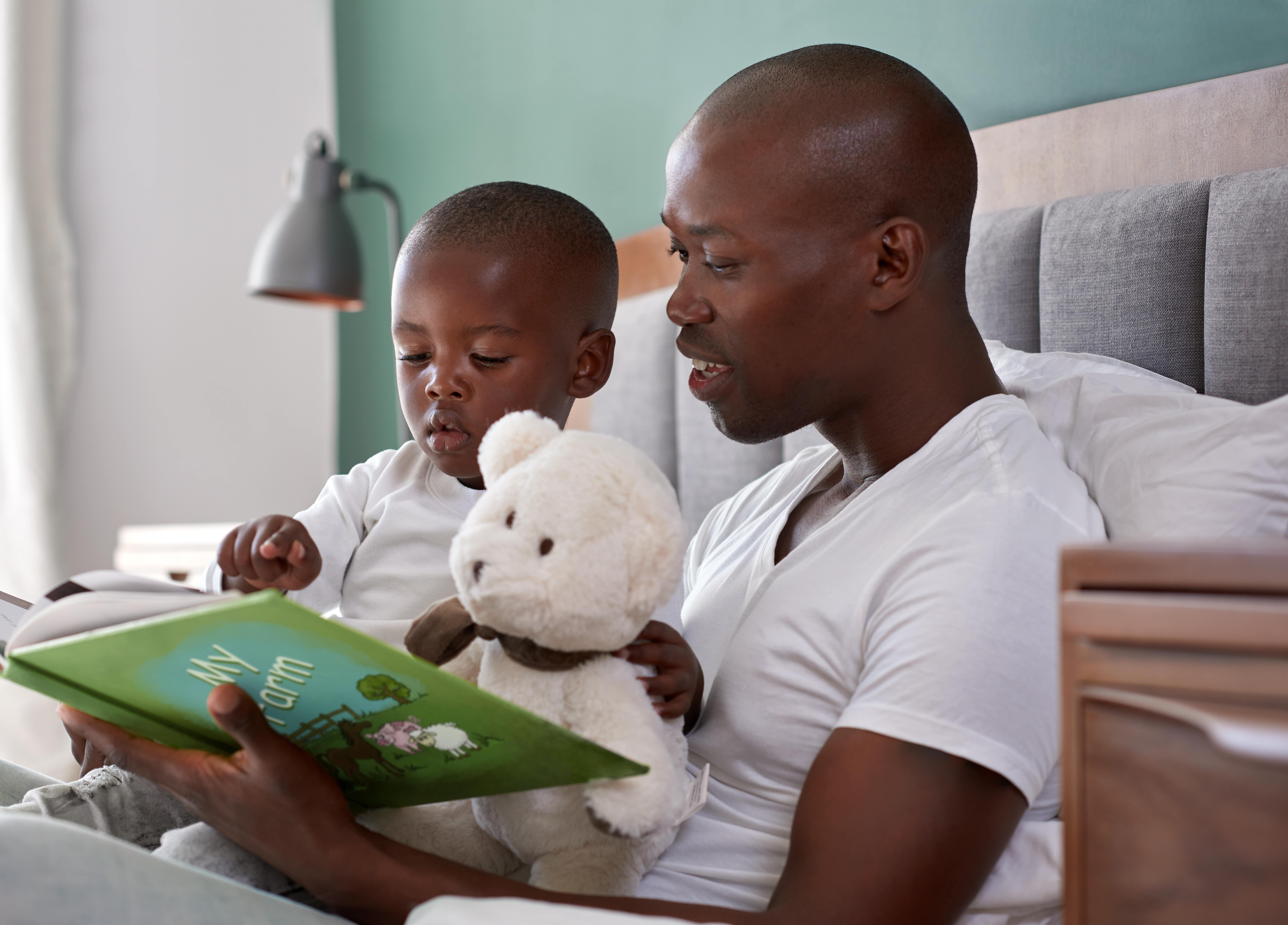 A dad and son reading a colourful picture book called My Farm in bed. They are cuddled close together and enjoying some one to one time together.