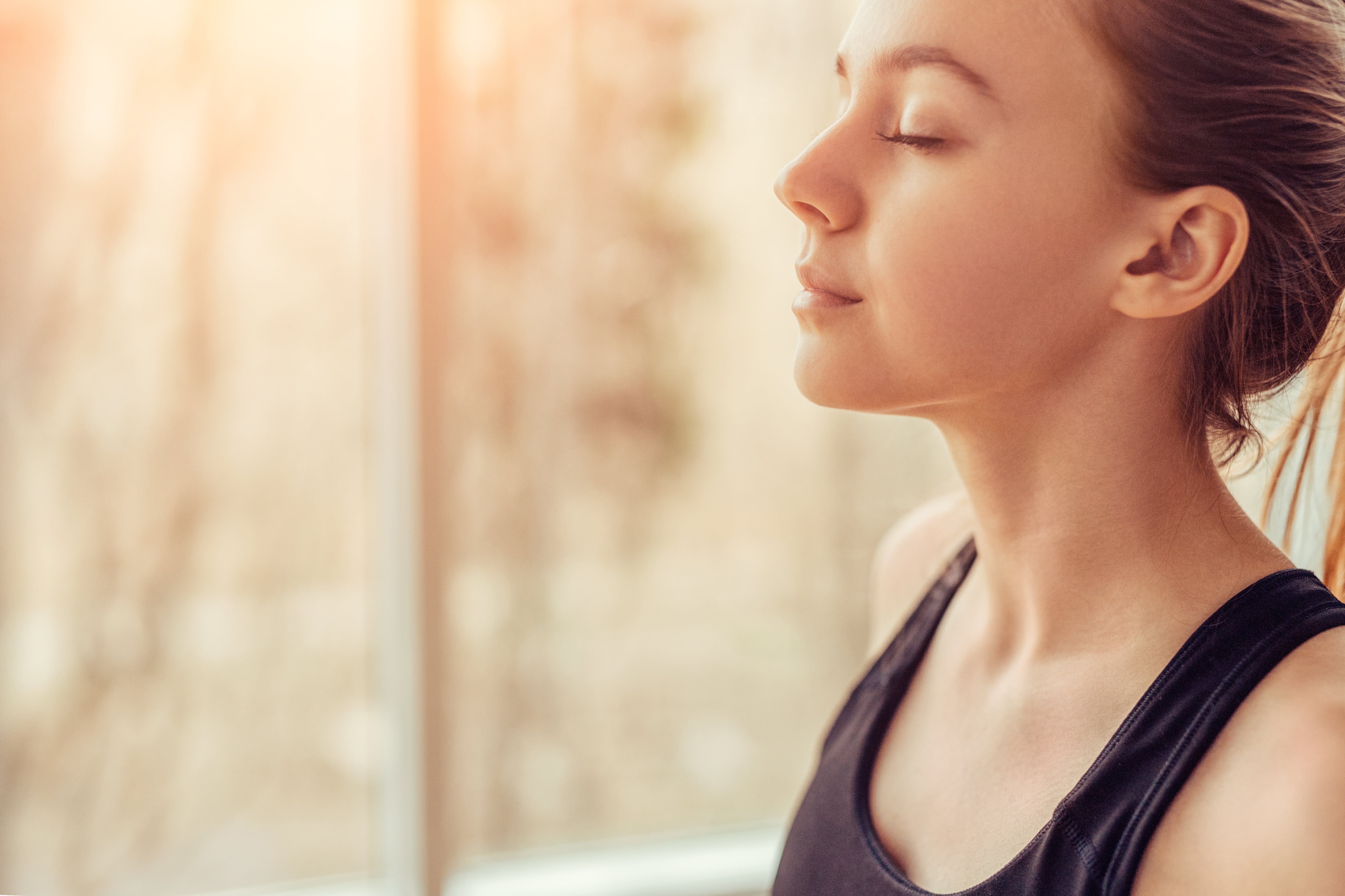 A lady practising mindful breathing exercises as the sunrise illuminates her face through the window.