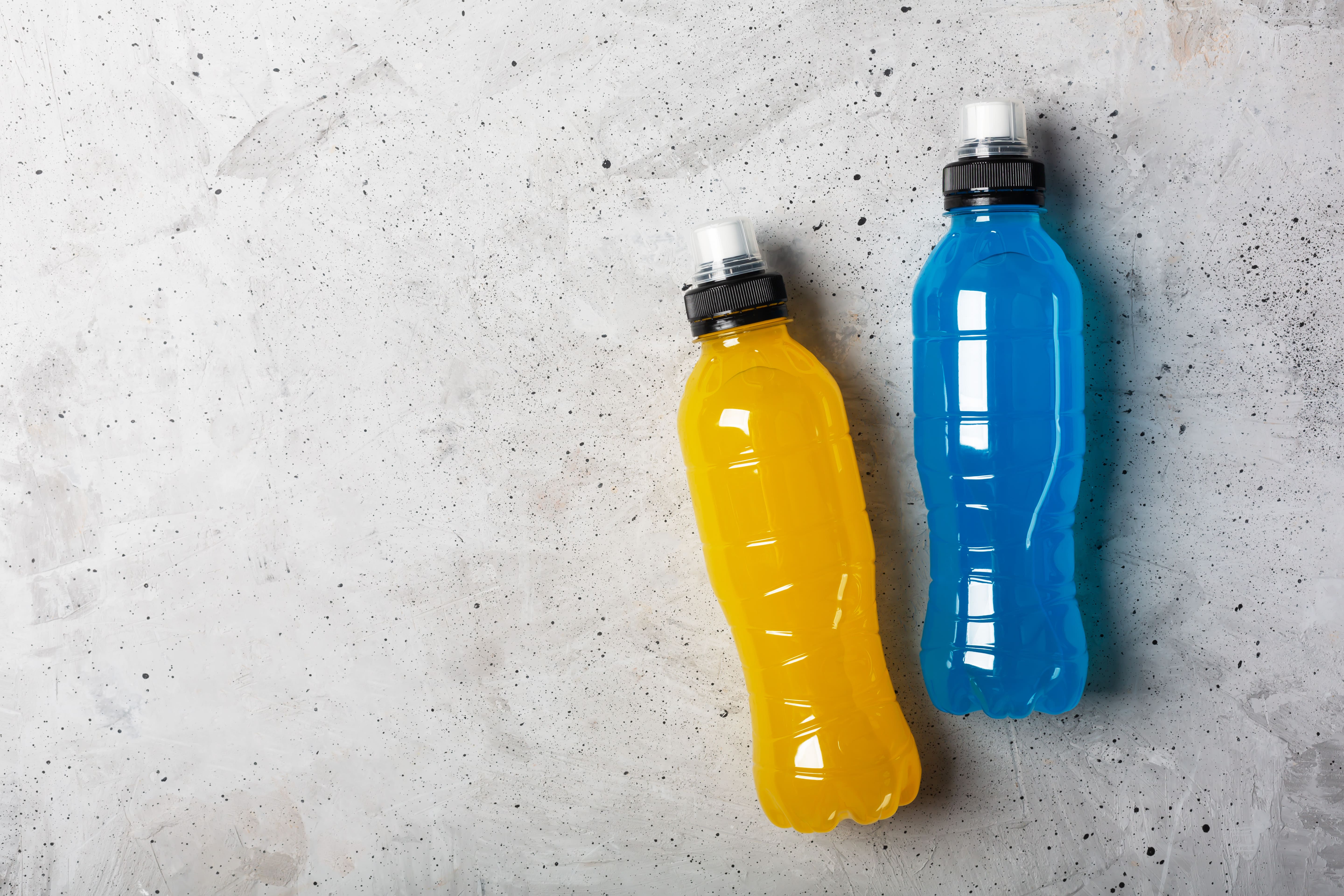 Two plastic bottles filled with energy drinks lie on their side on a granite kitchen surface. One is blue and one is orange.
