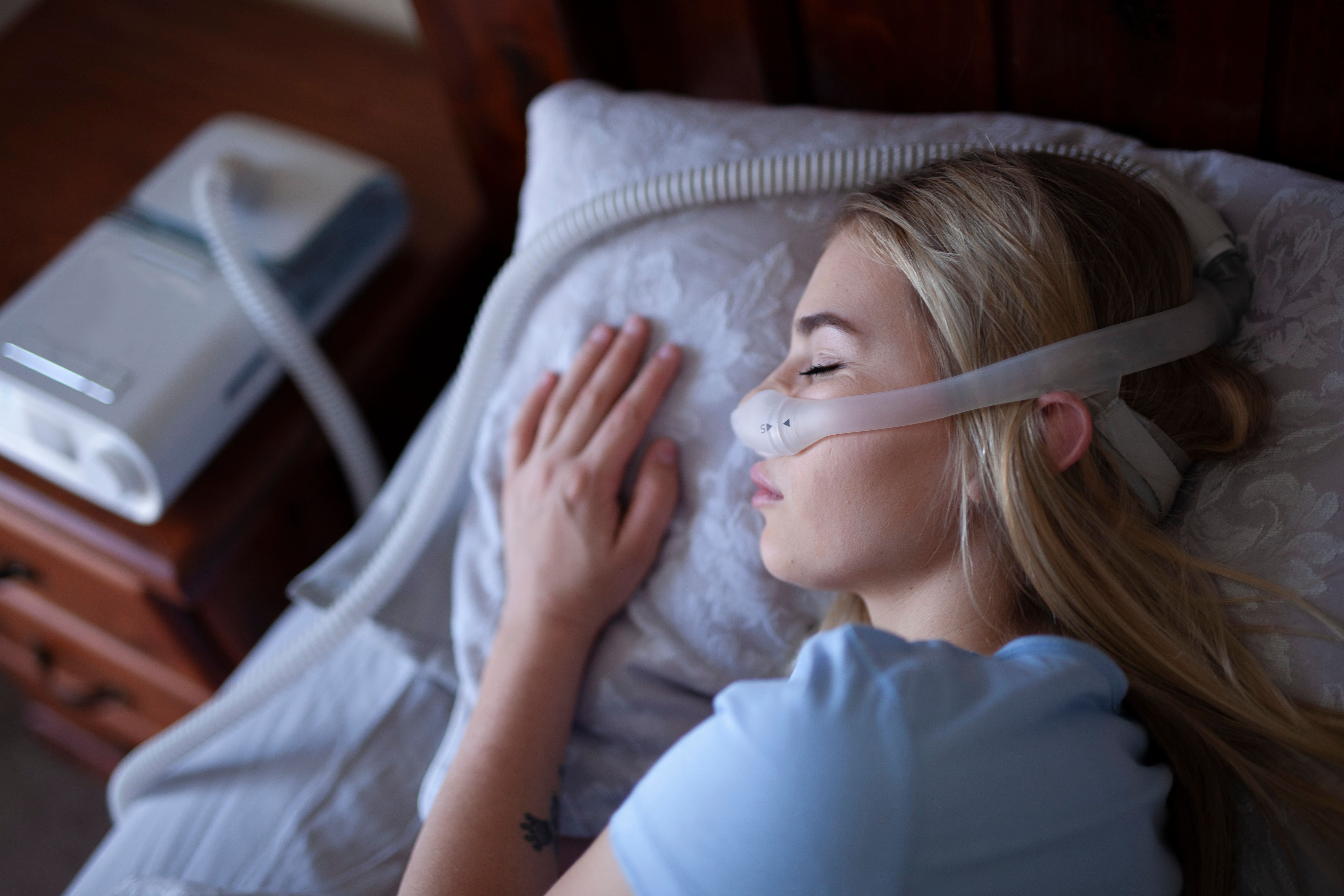 Woman asleep on her side in bed using a CPAP machine.