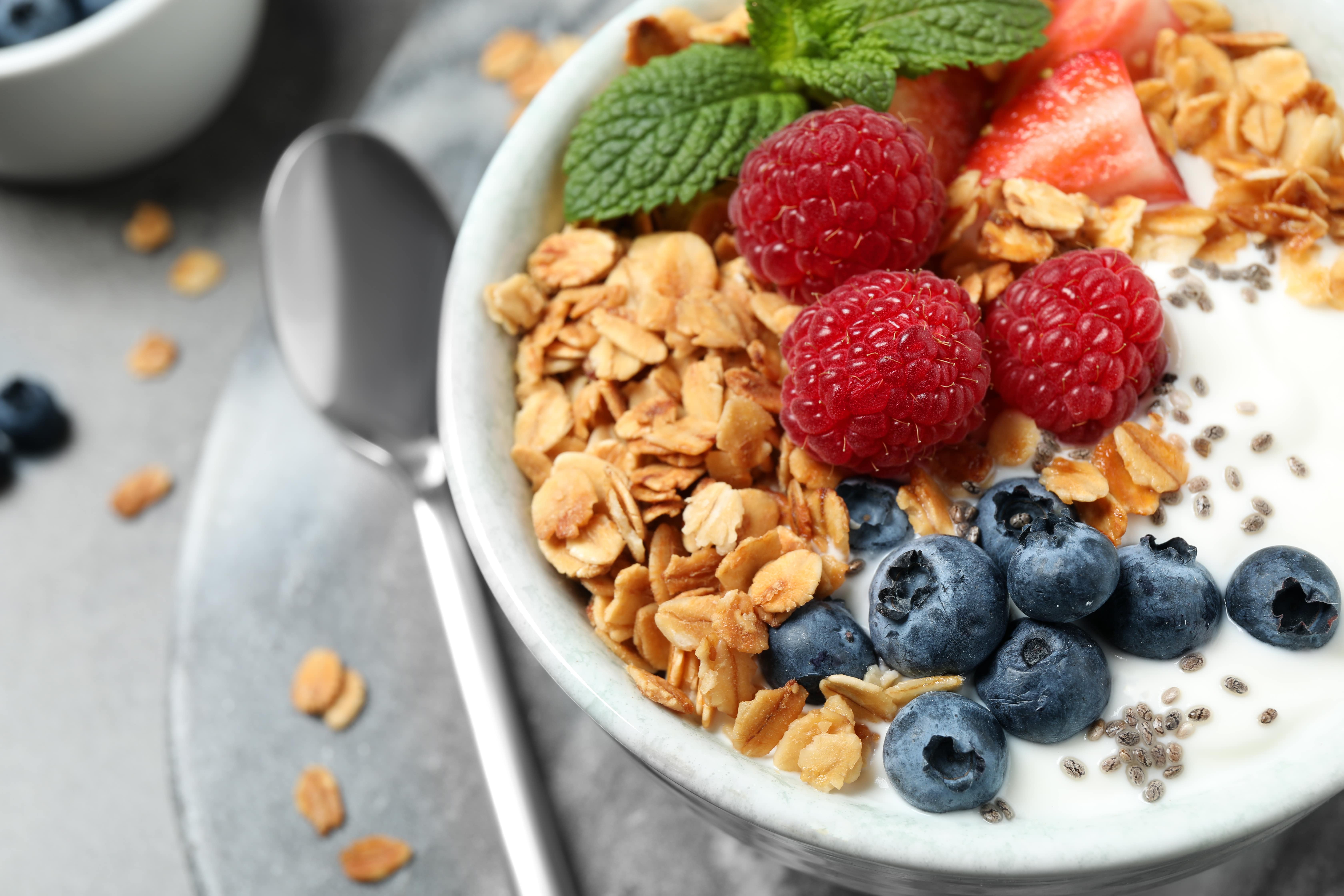 A bowl filled with granola, milk, berries and a sprig of mint with a large spoon beside it.