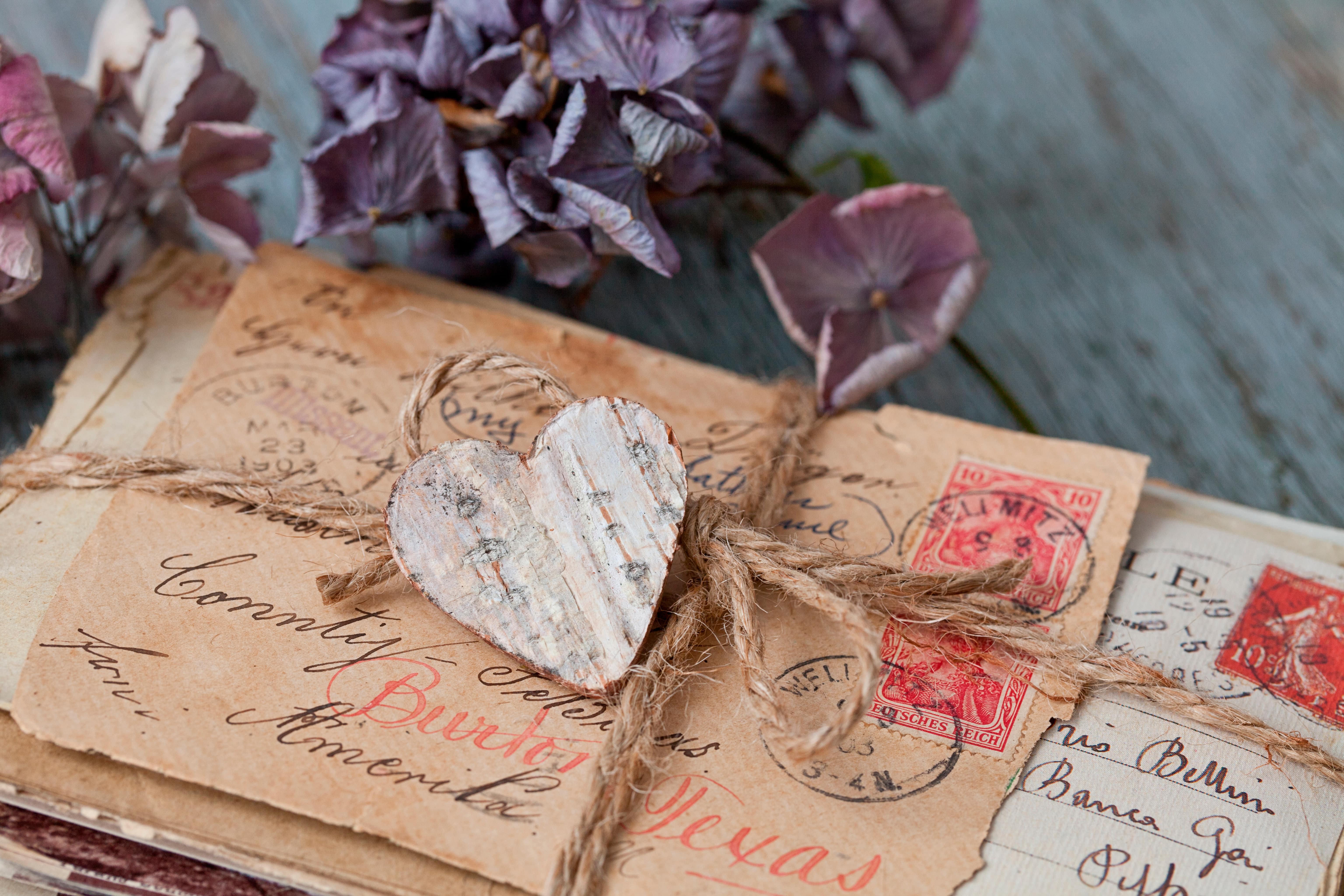 A bundle of old letters tied with string and a wooden heart on top. posies of hydrangeas lie next to the ltters.