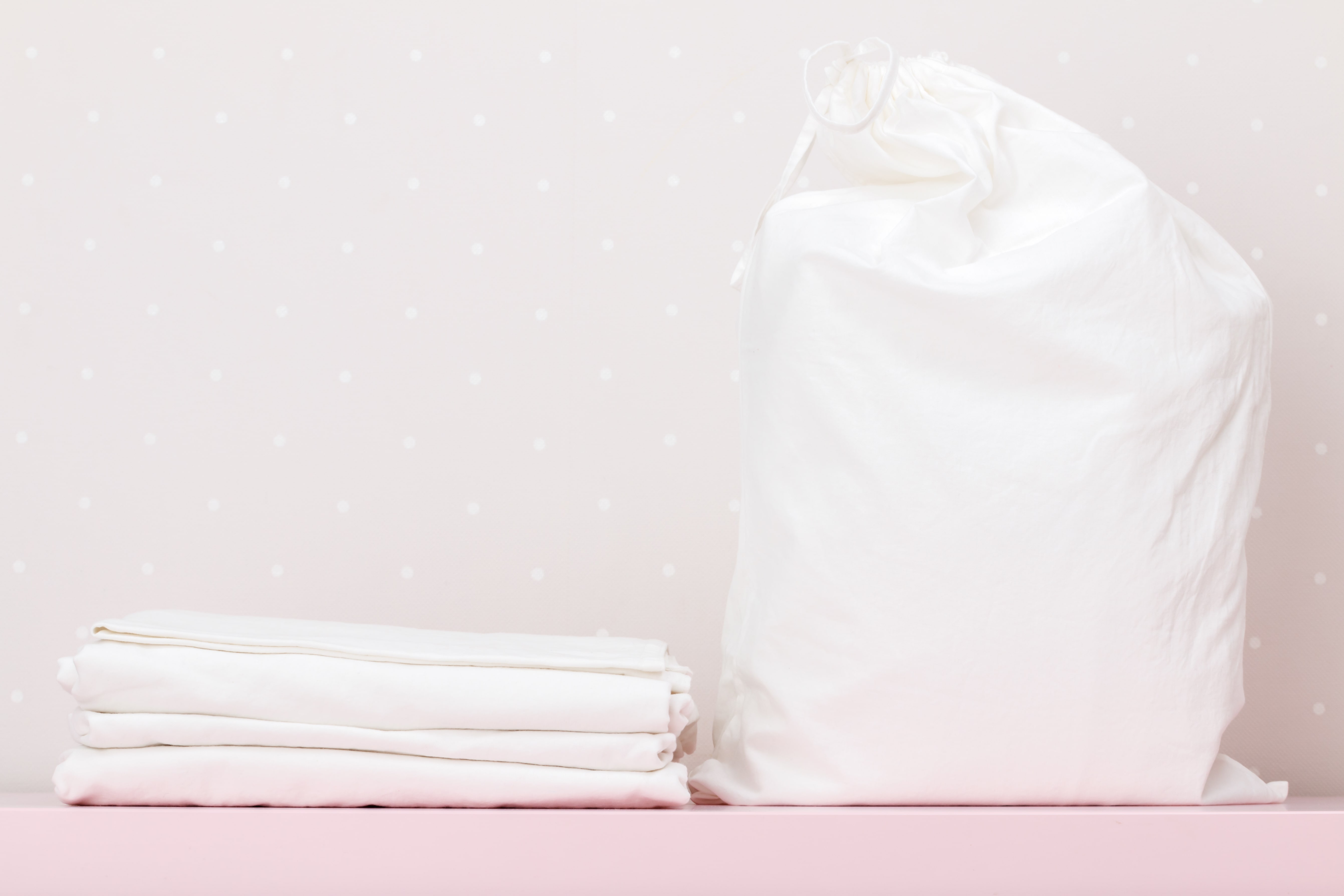 A duvet stored in a breathable bag. Some bedsheets are piled neatly next to the duvet bag.