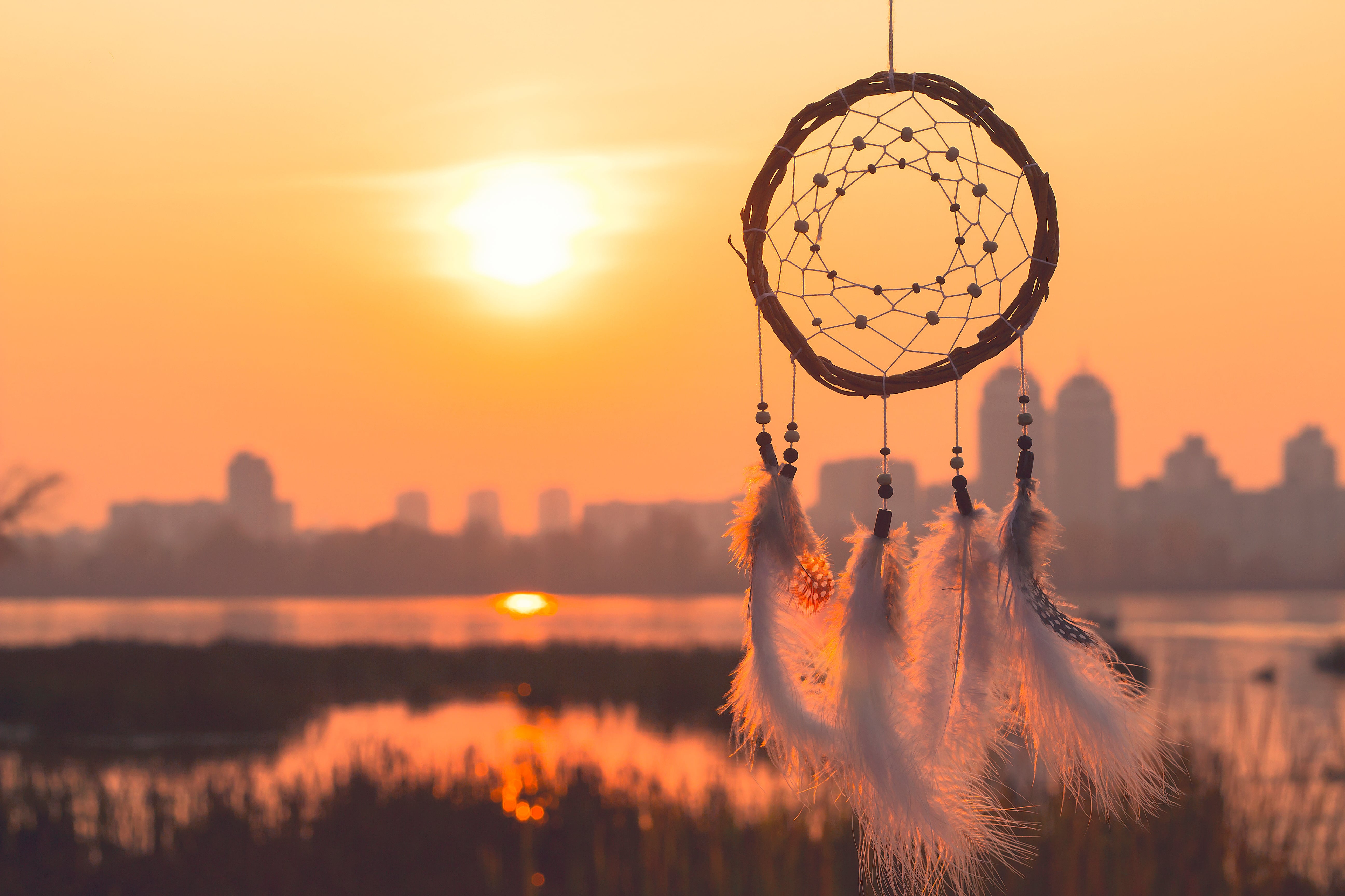 A dream catcher silhouetted against a cityscape at sunset.