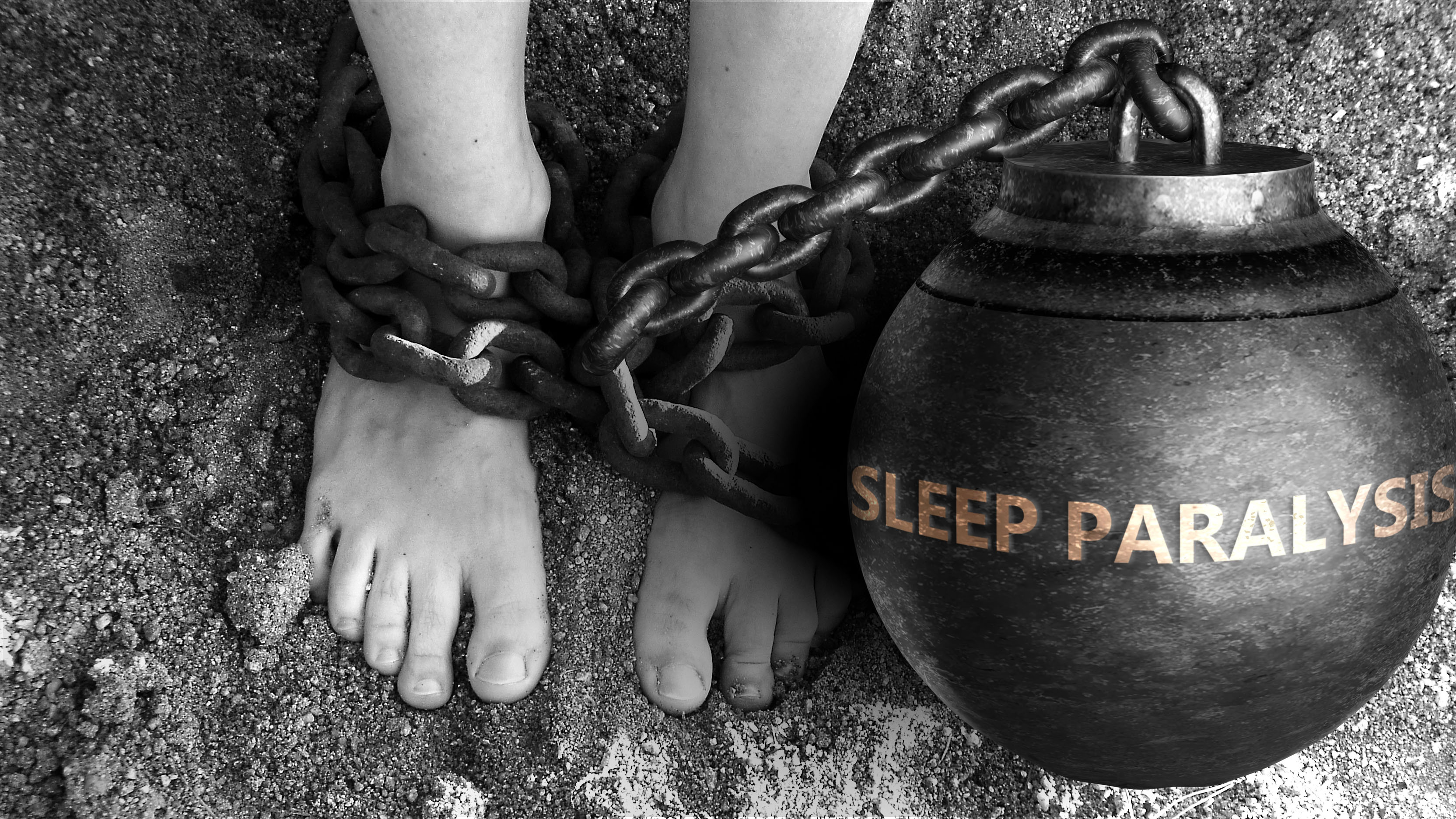 Two bare feet in the sand tethered together with a ball and chain embossed with the words Sleep Paralysis