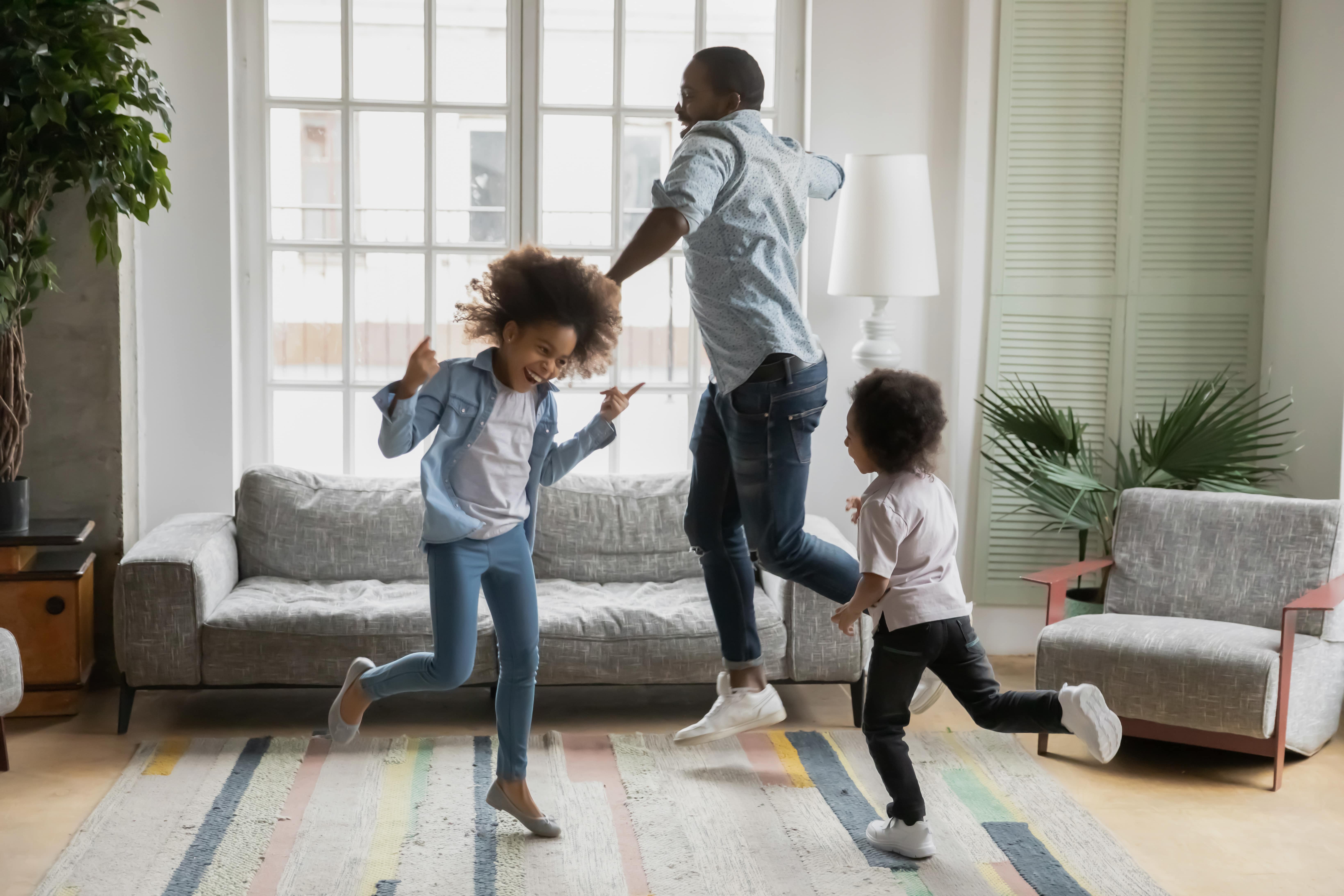 A father dancing freely around the living room with his two children as they listen to music and dance away some of their unspent energy.
