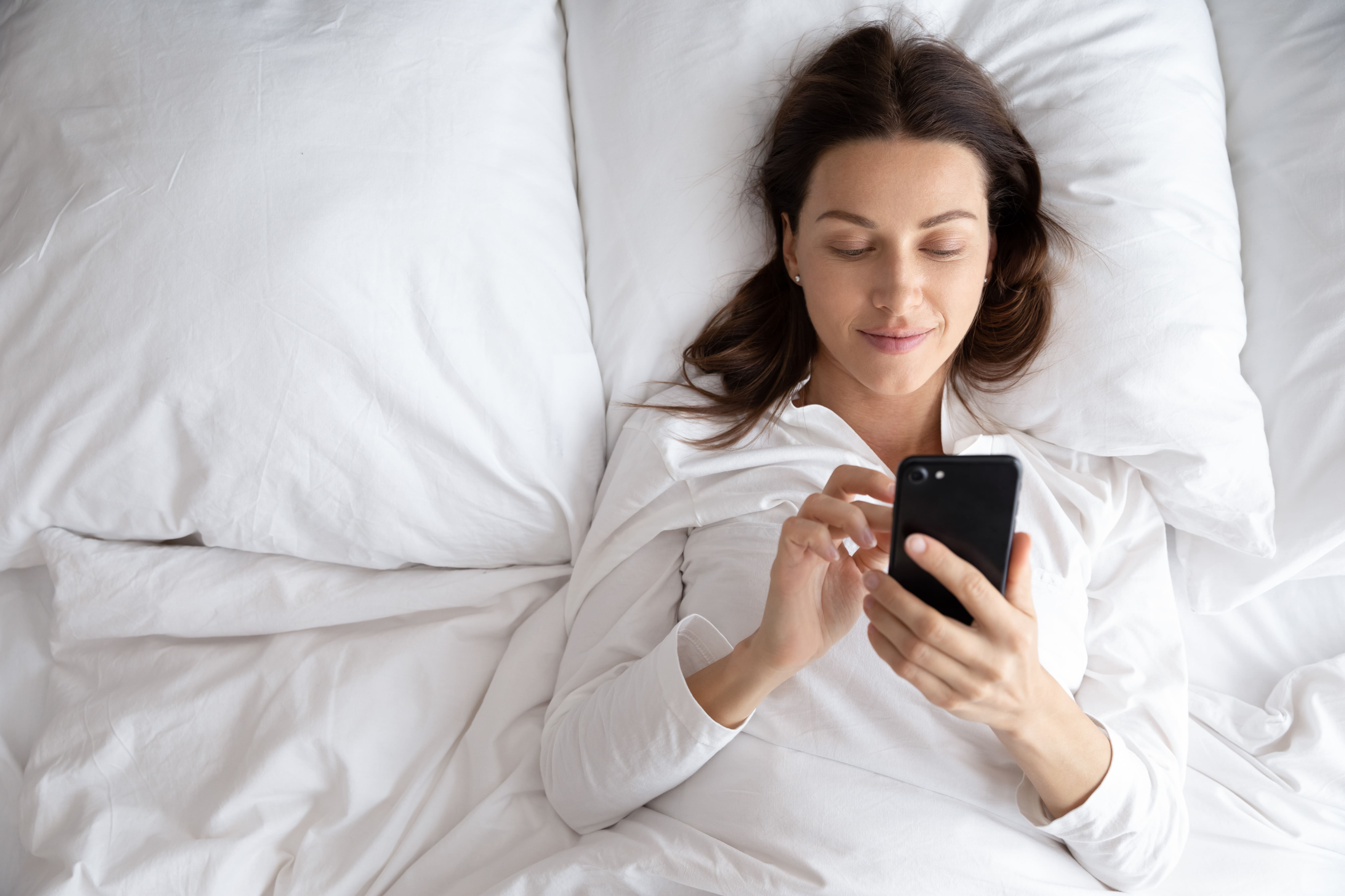 Bird's eye view of woman lying bed scrolling on her mobile 'phone.