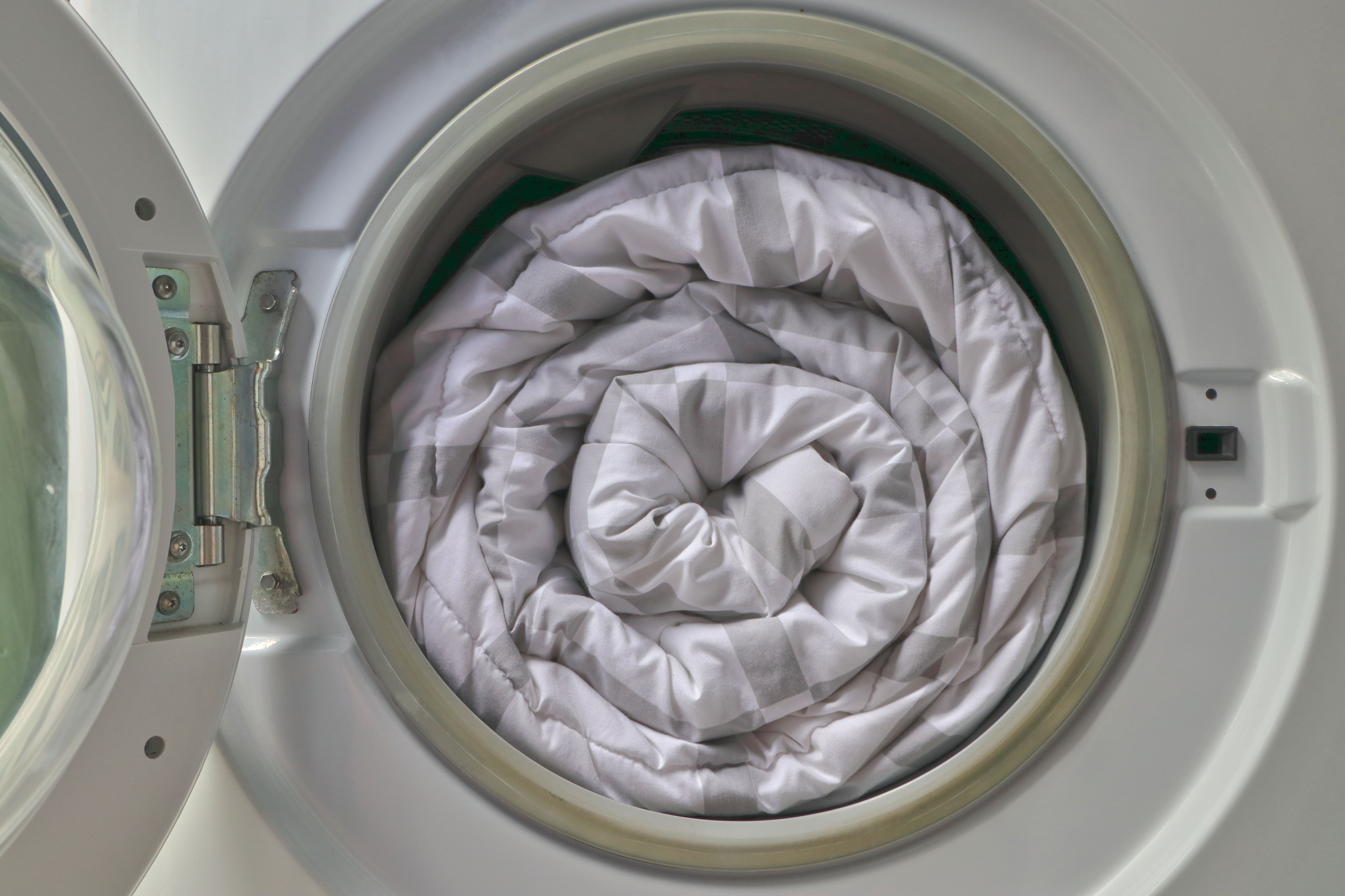 An open washing machine reveals a rolled up duvet inside.