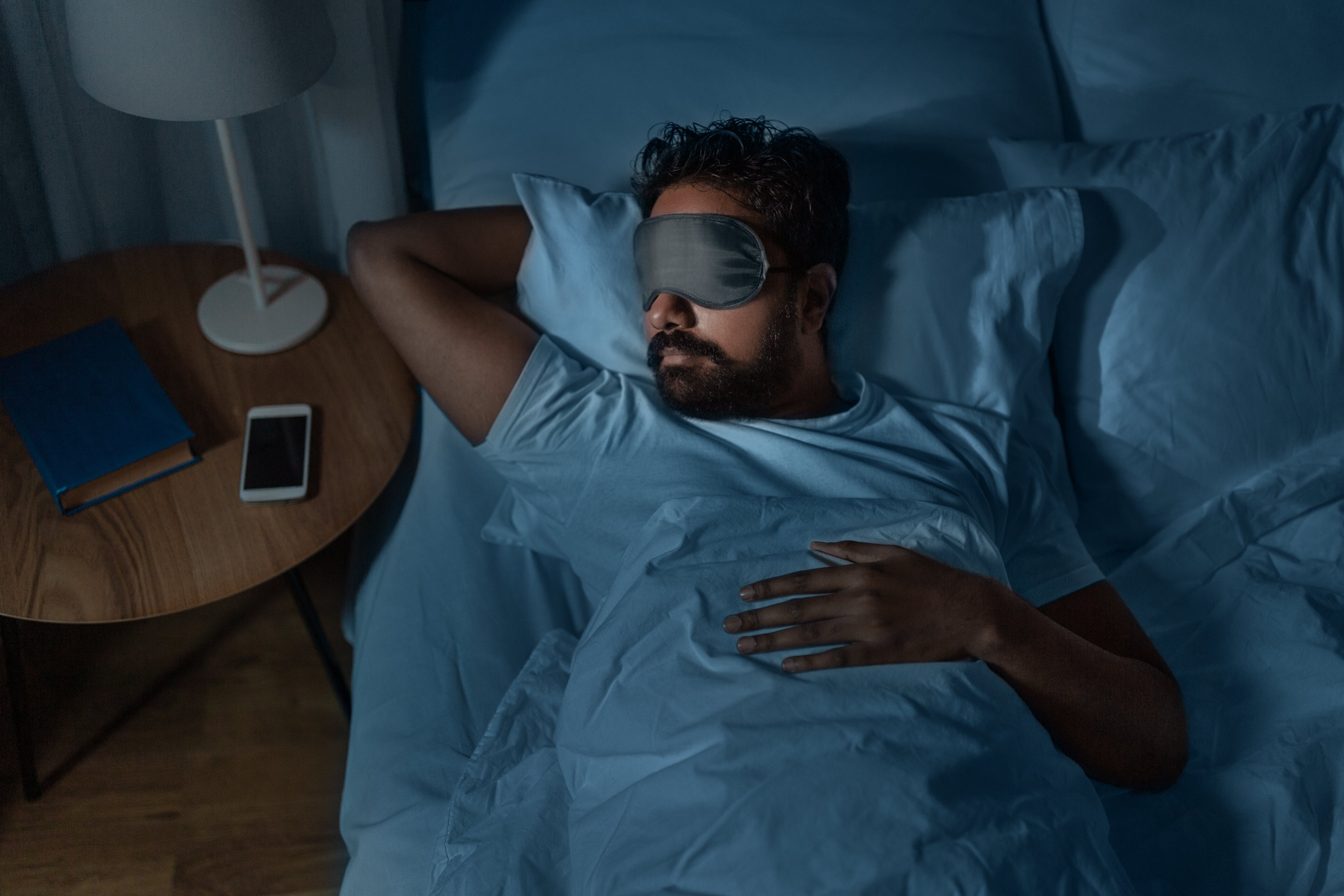 A man wears an eye mask as he sleeps in bed.