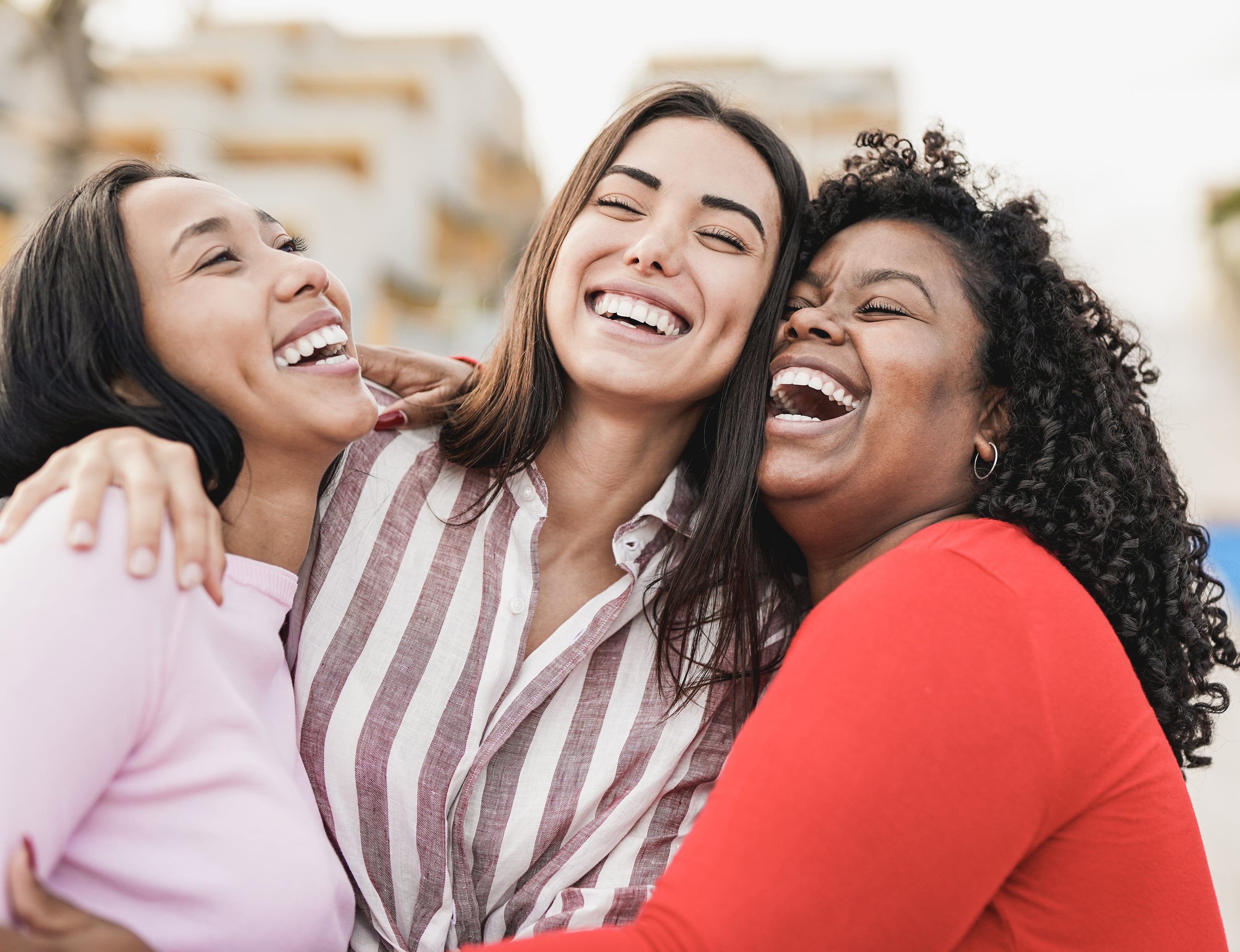 Three women are clutched in an embrace as they laugh.