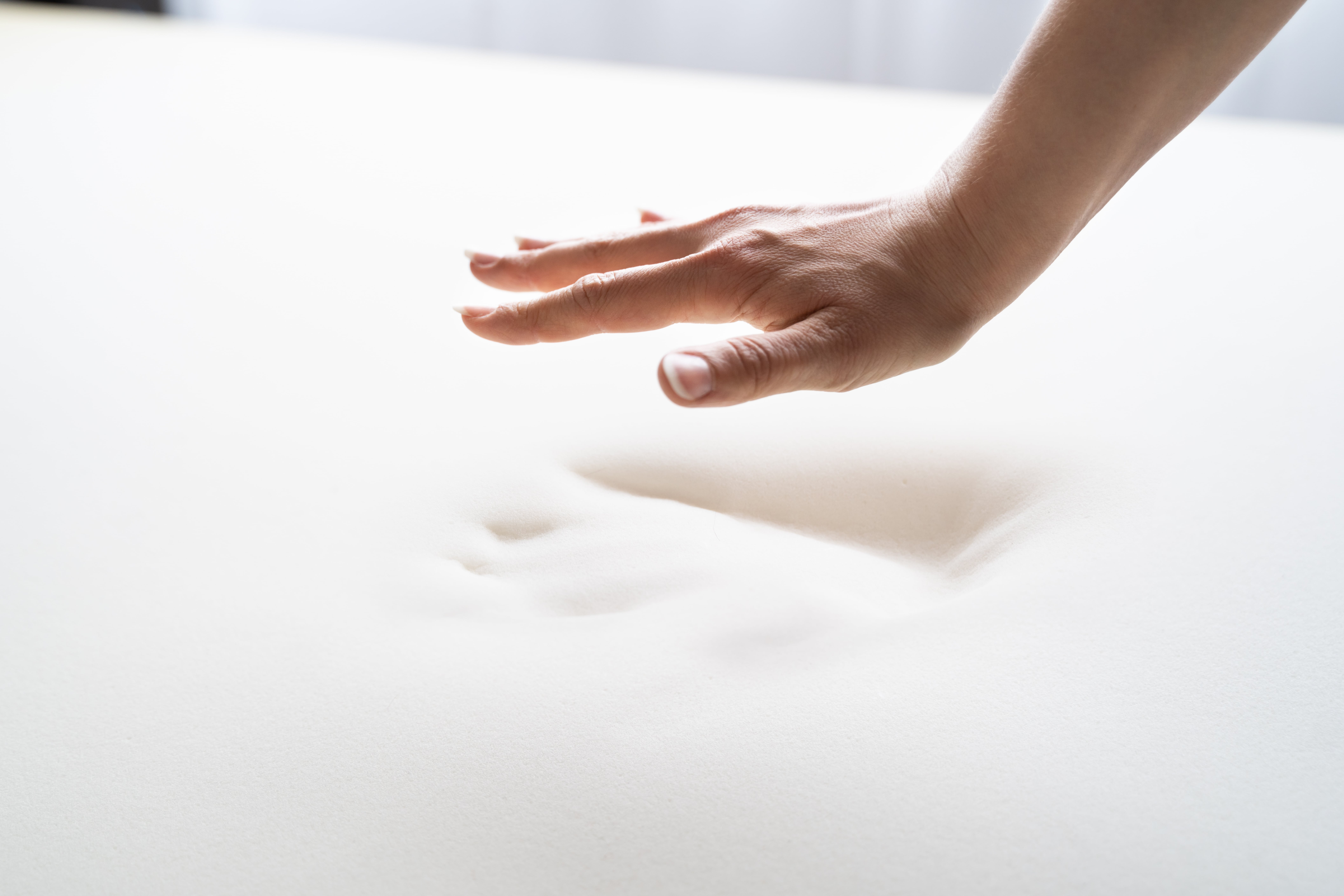 a memory foam mattress with an imprint of a hand with hand and partial arm retreating from mattress.