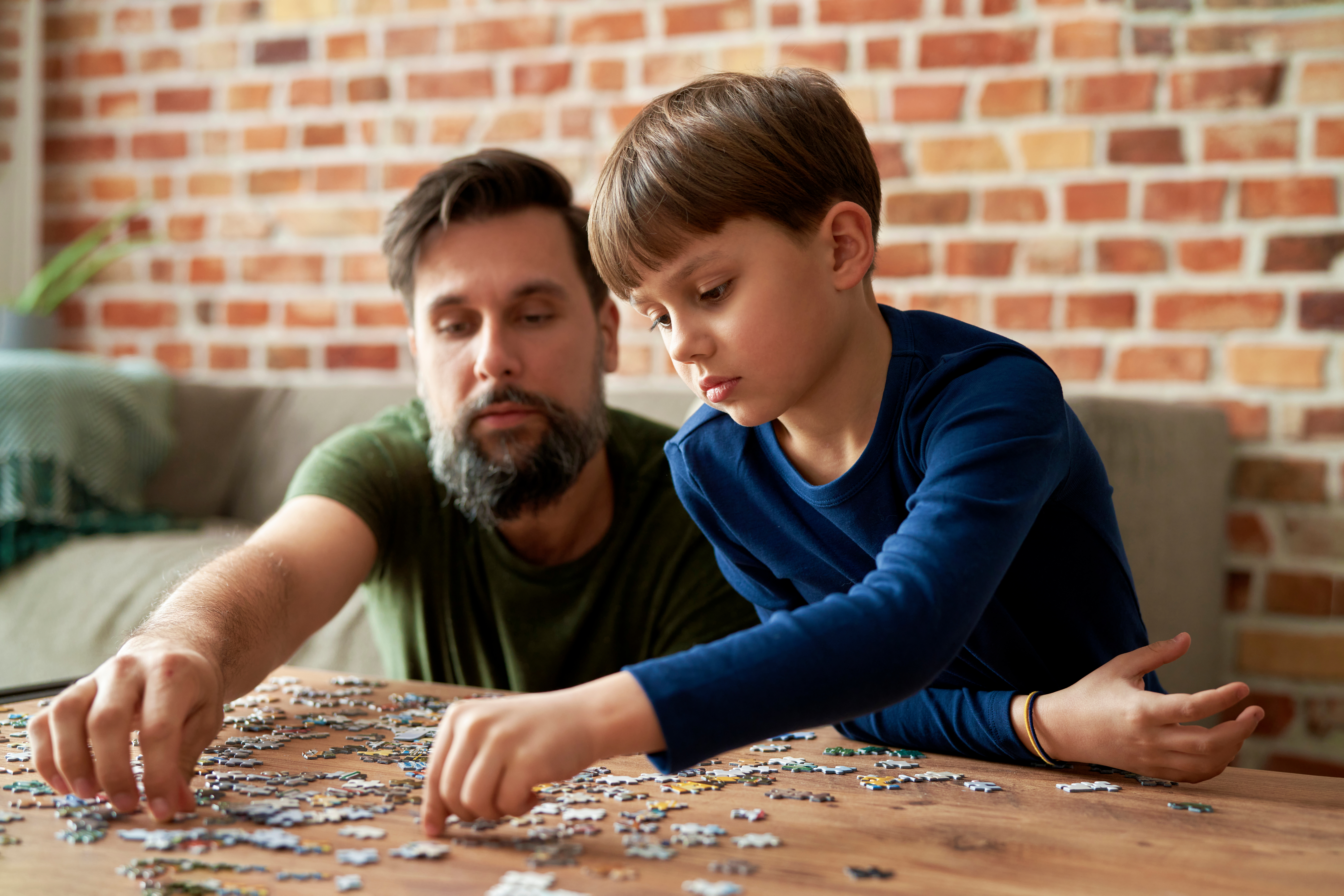 A father and son deep in concentration as they try to connect the pieces of a challenging jigsaw puzzle