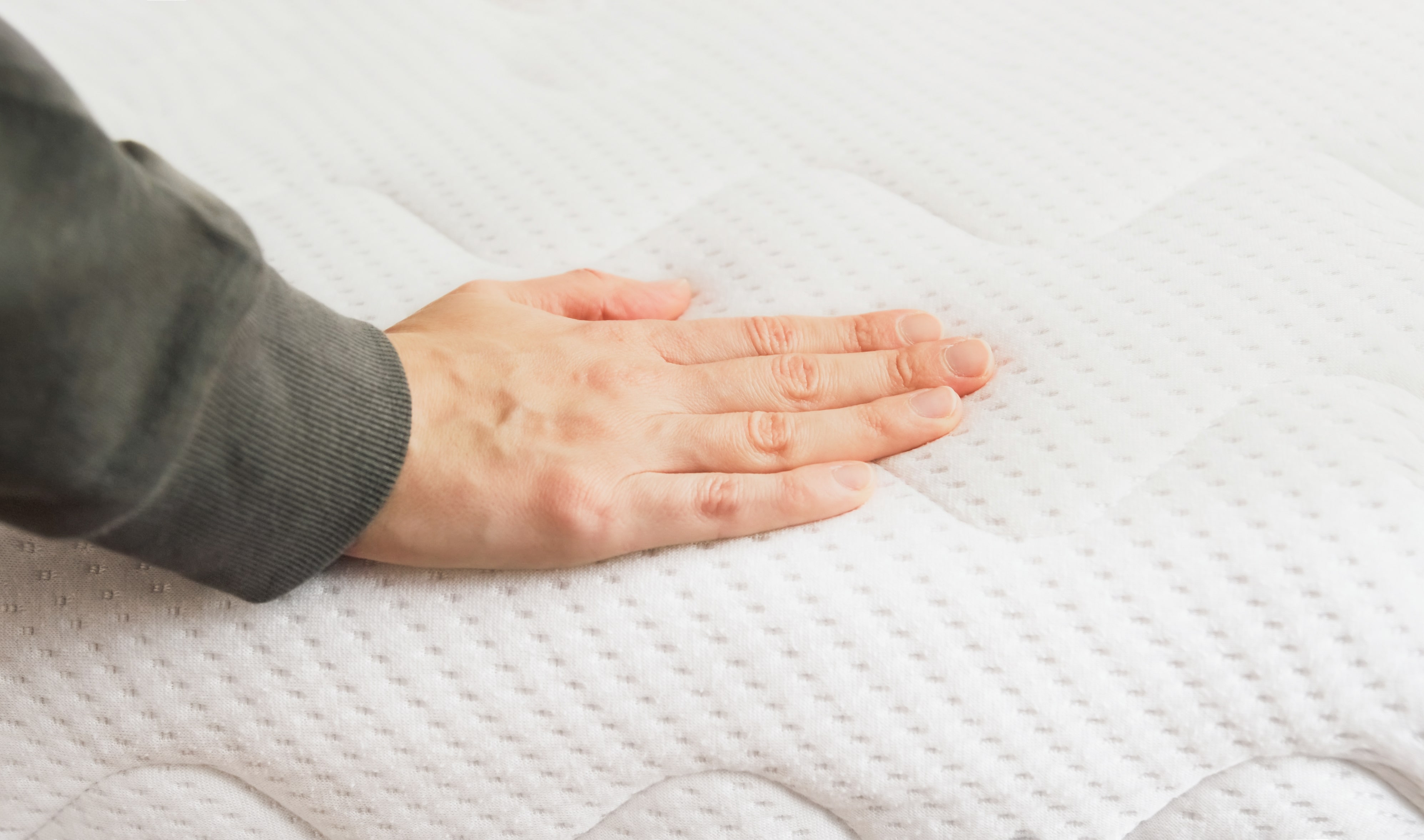A person pushing on a mattress to test out the firmness and comfort level of it.