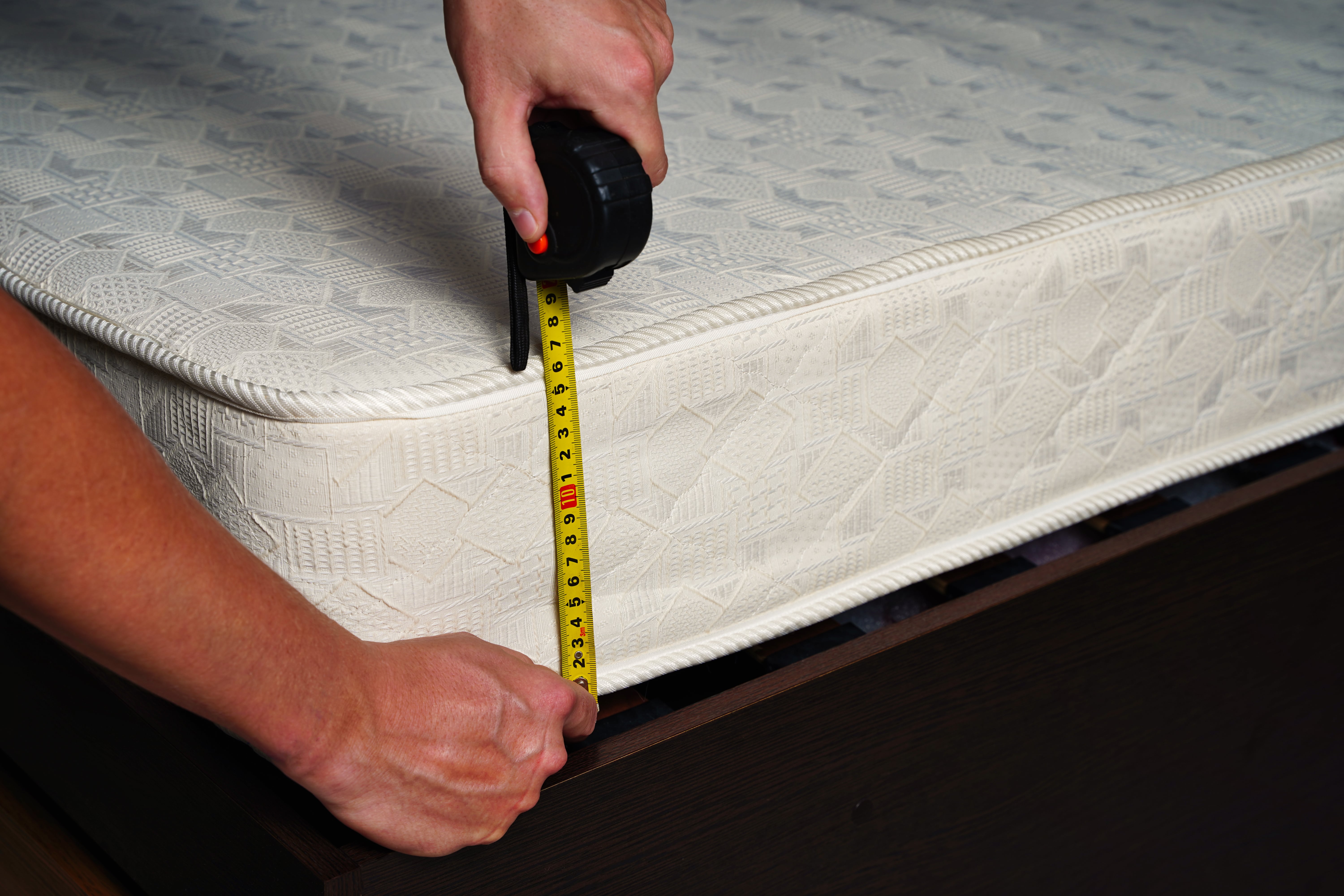 A person using a tape measure to measure the depth of their mattress