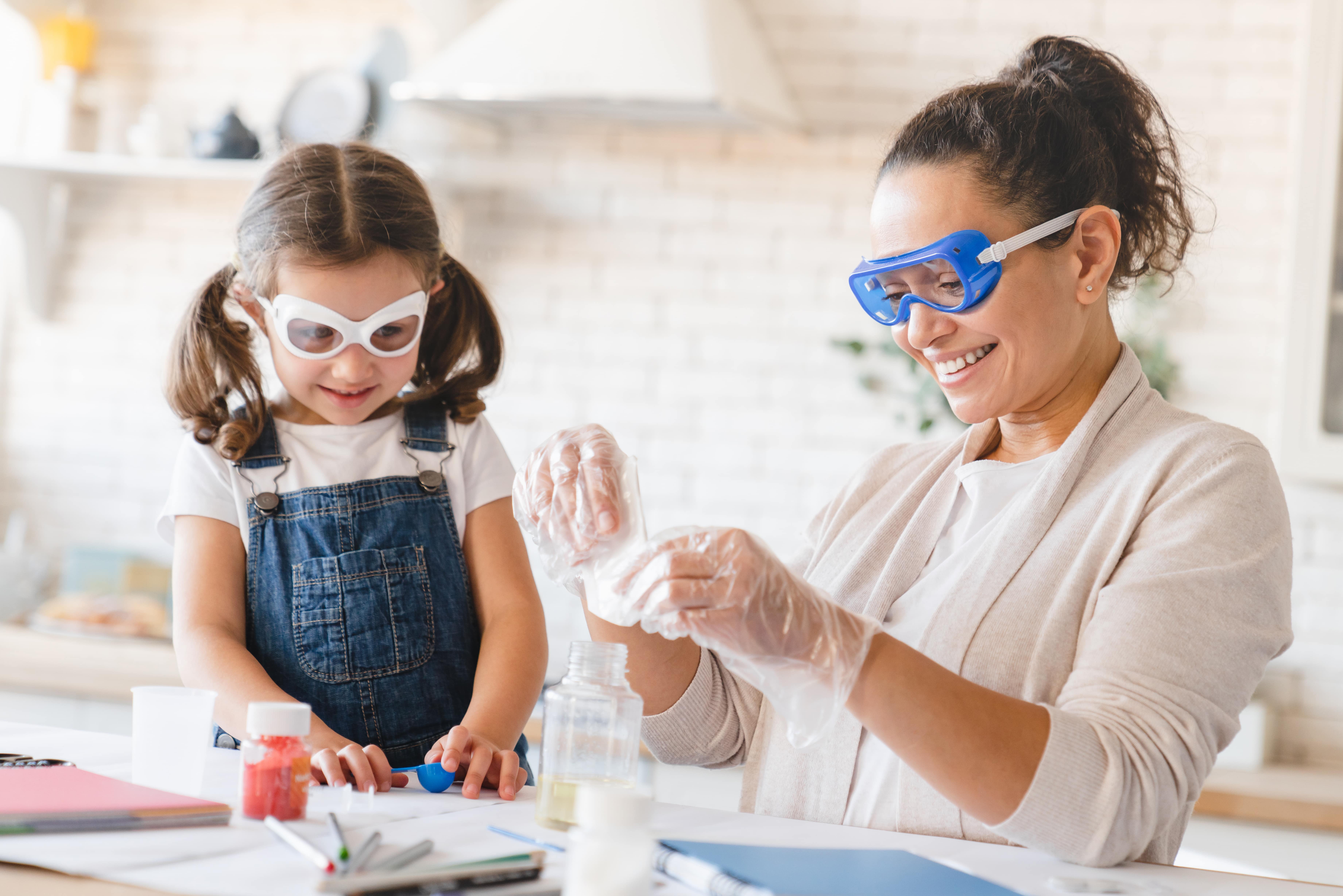 A mum and daughter wearing safety goggles and gloves while conducting science experiments at home.