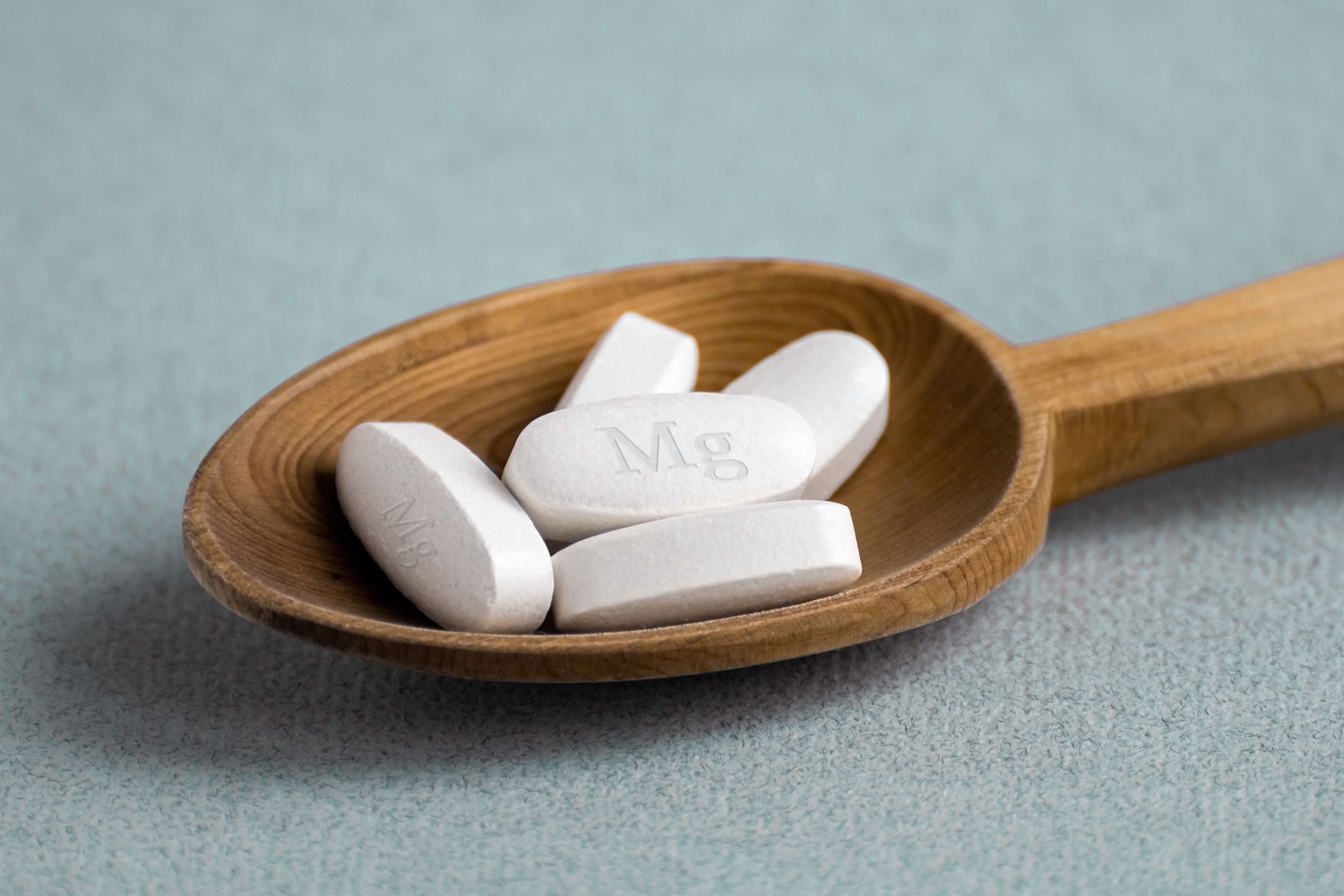 5 white magnesium supplements in tablet form on a wooden spoon
