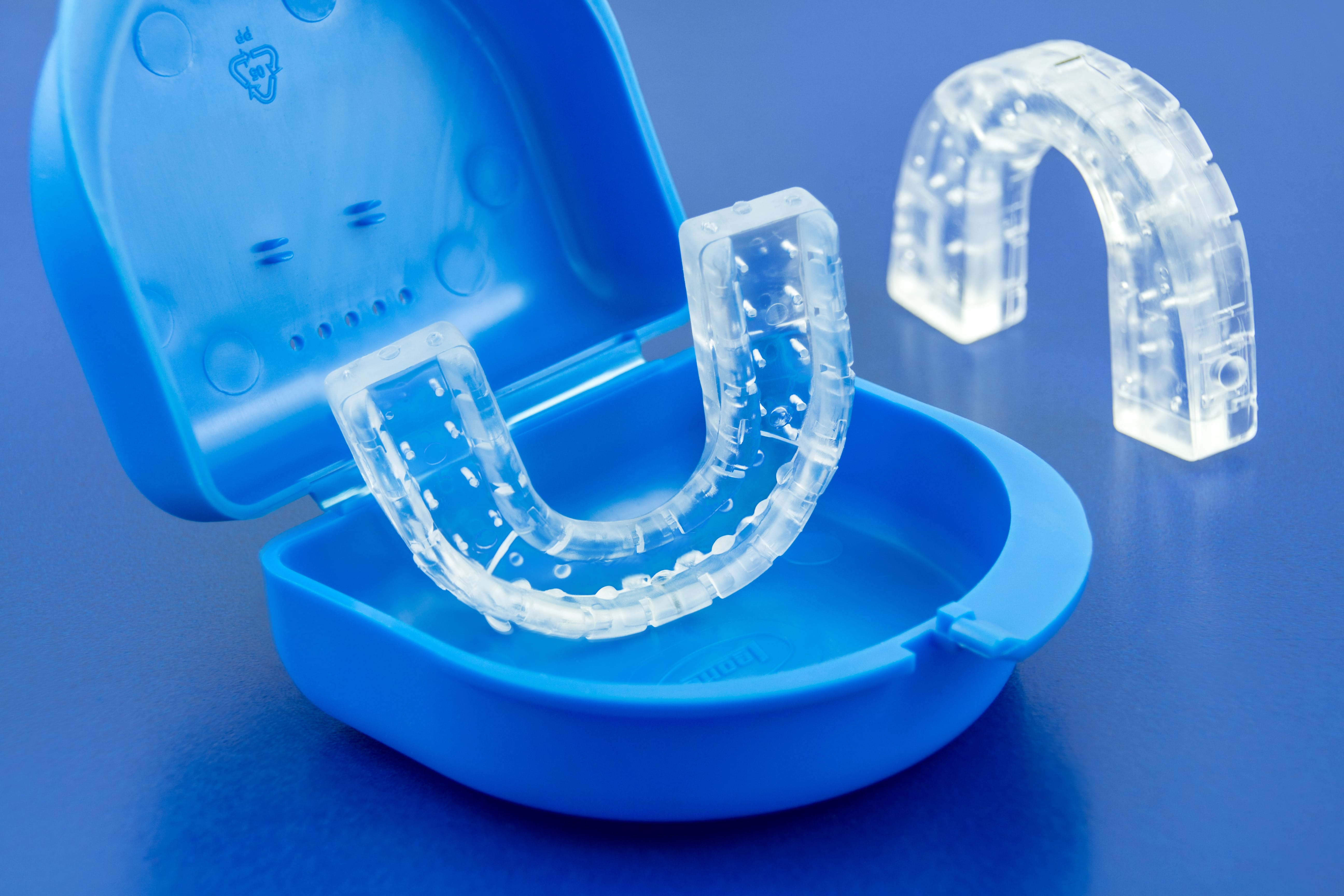 An open box contains what appears to be a gum shield for a row of teeth. The other section of the gum shield stands beside the box.
