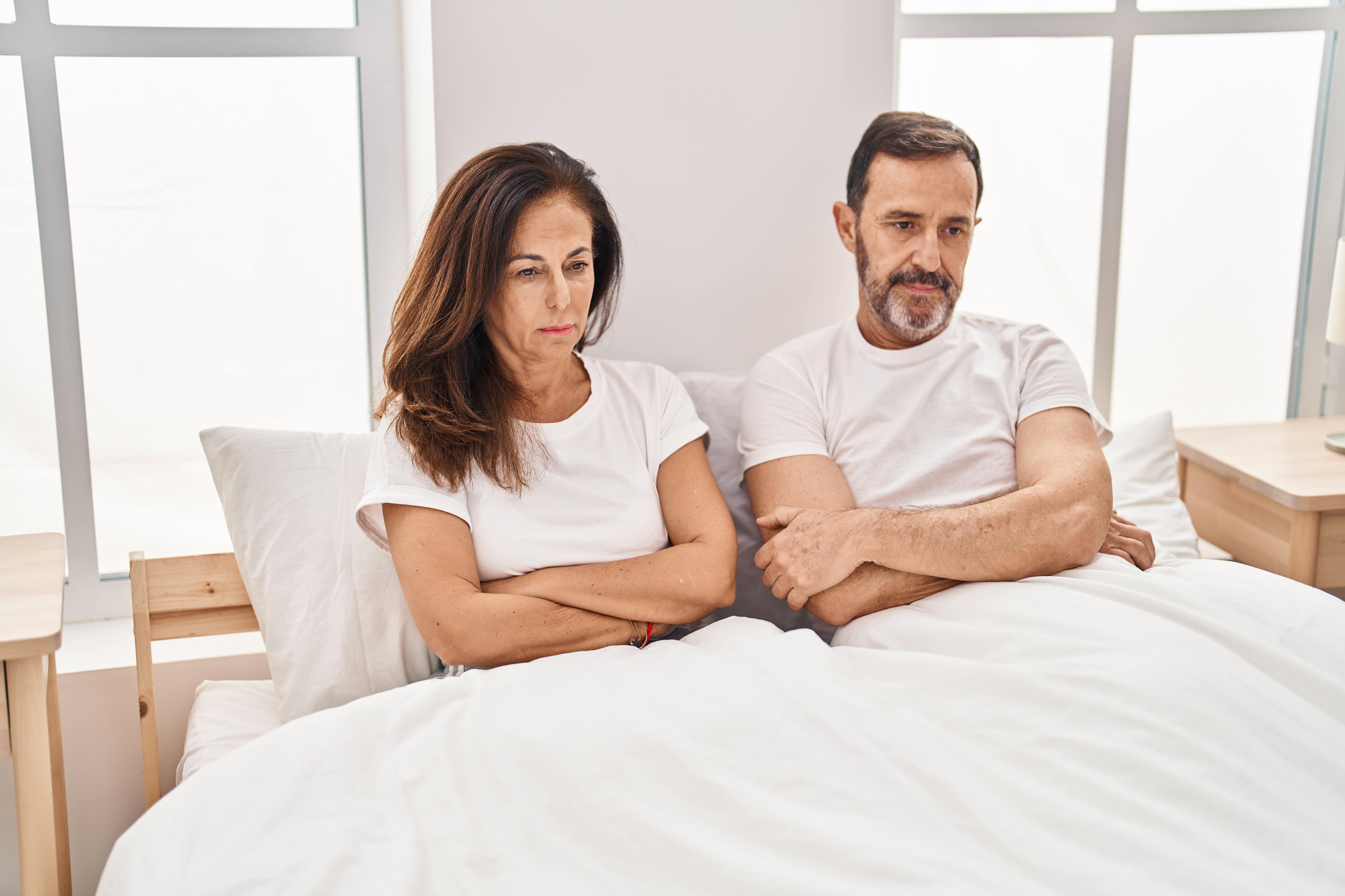 Middle-aged man and woman sitting up in bed with arms crossed looking unhappy