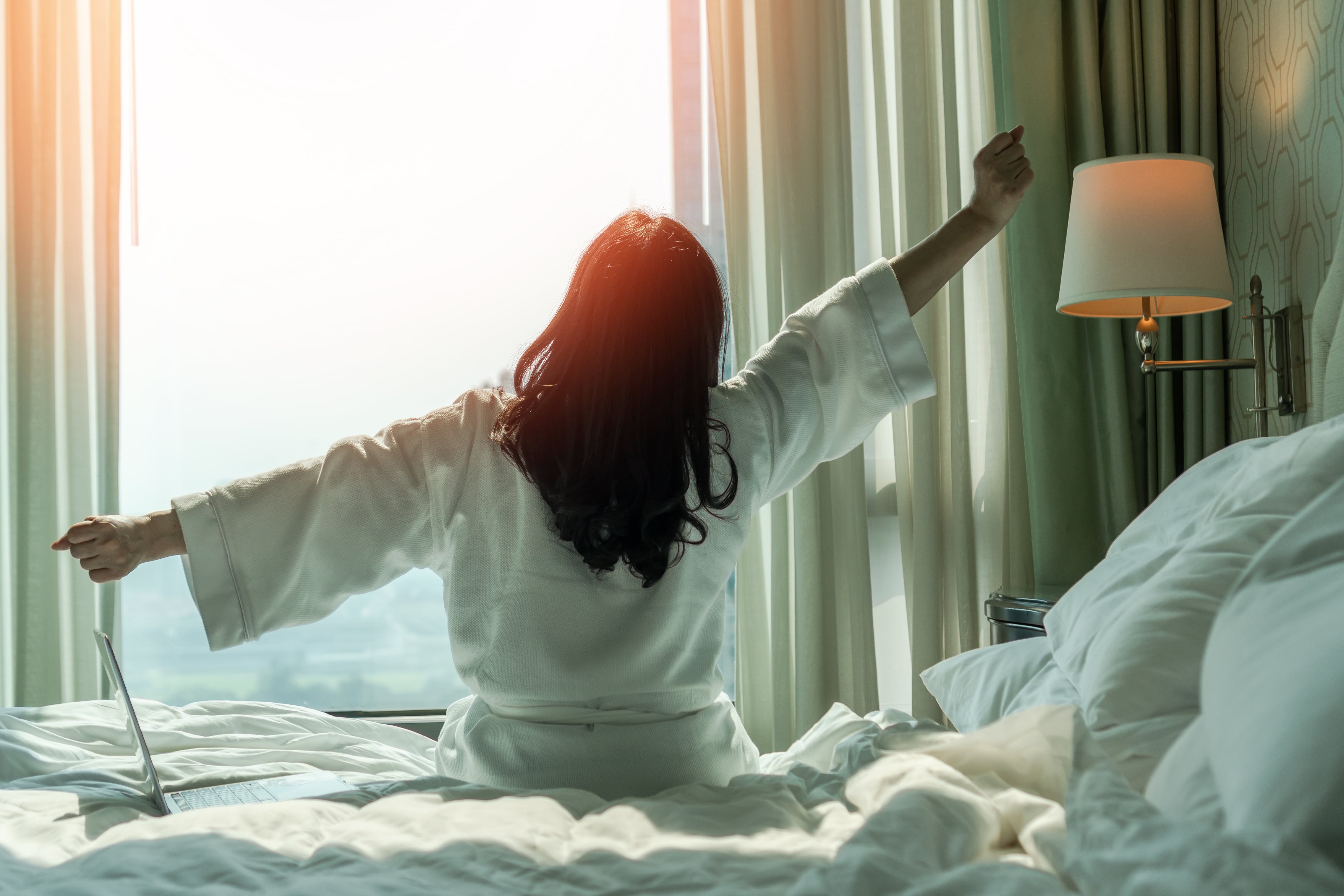 A lady stretching as she wakes up to the warmth of the sun rise through her bedroom window