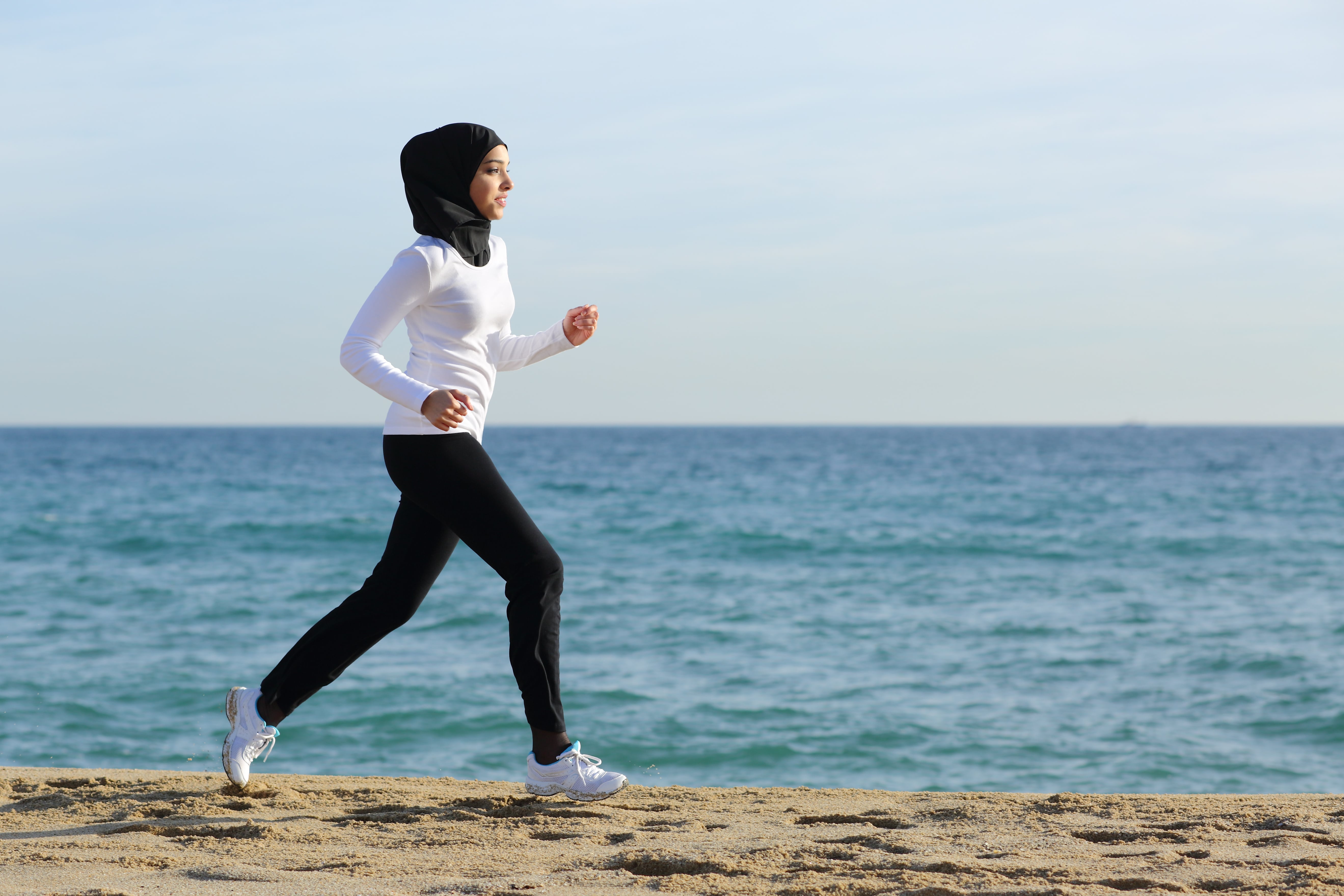 Woman jogging on a beach next to the shoreline.
