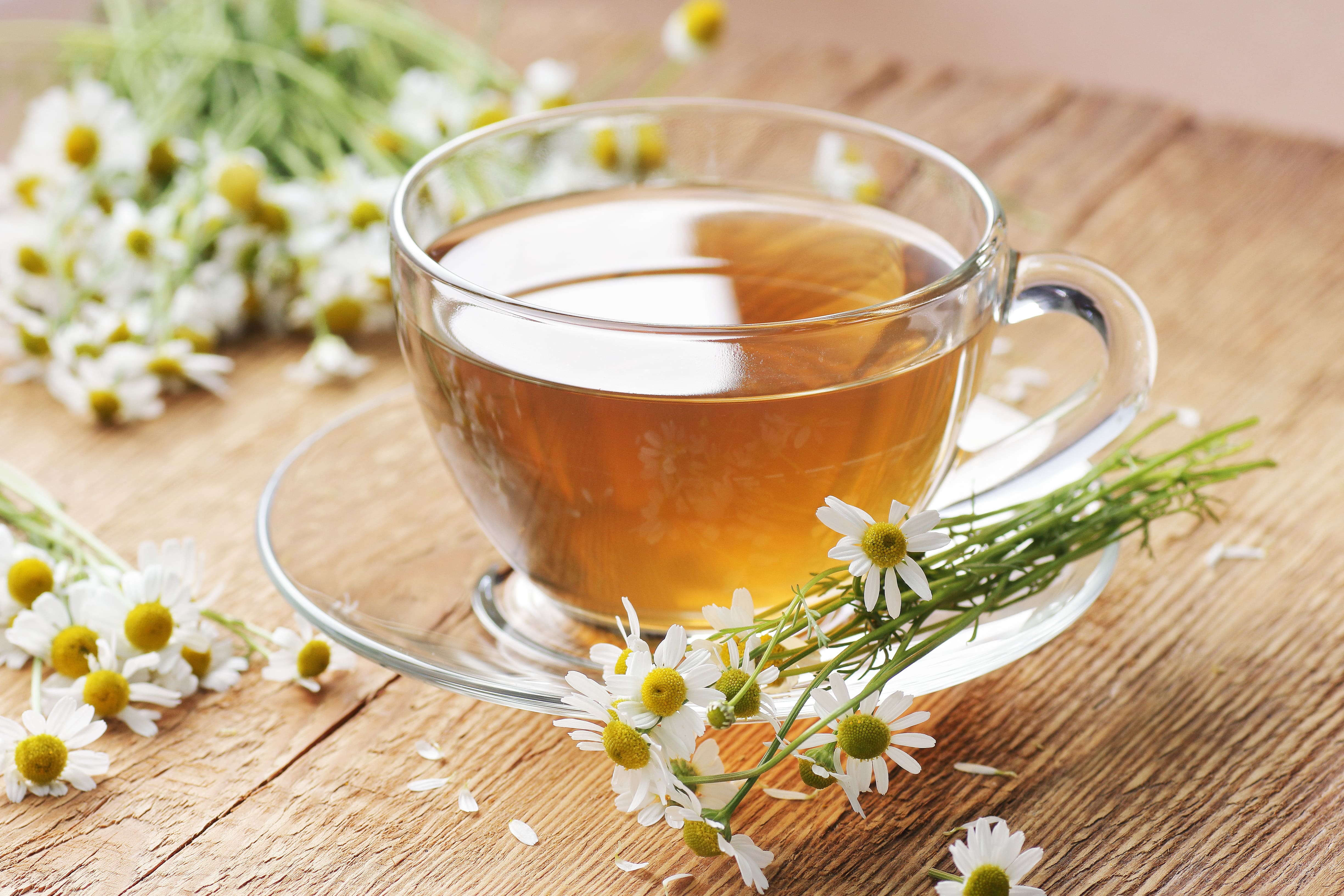A glass mug of chamomile tea, another natural sleep remedy, with chamomile flowers scattered on the saucer and the table top
