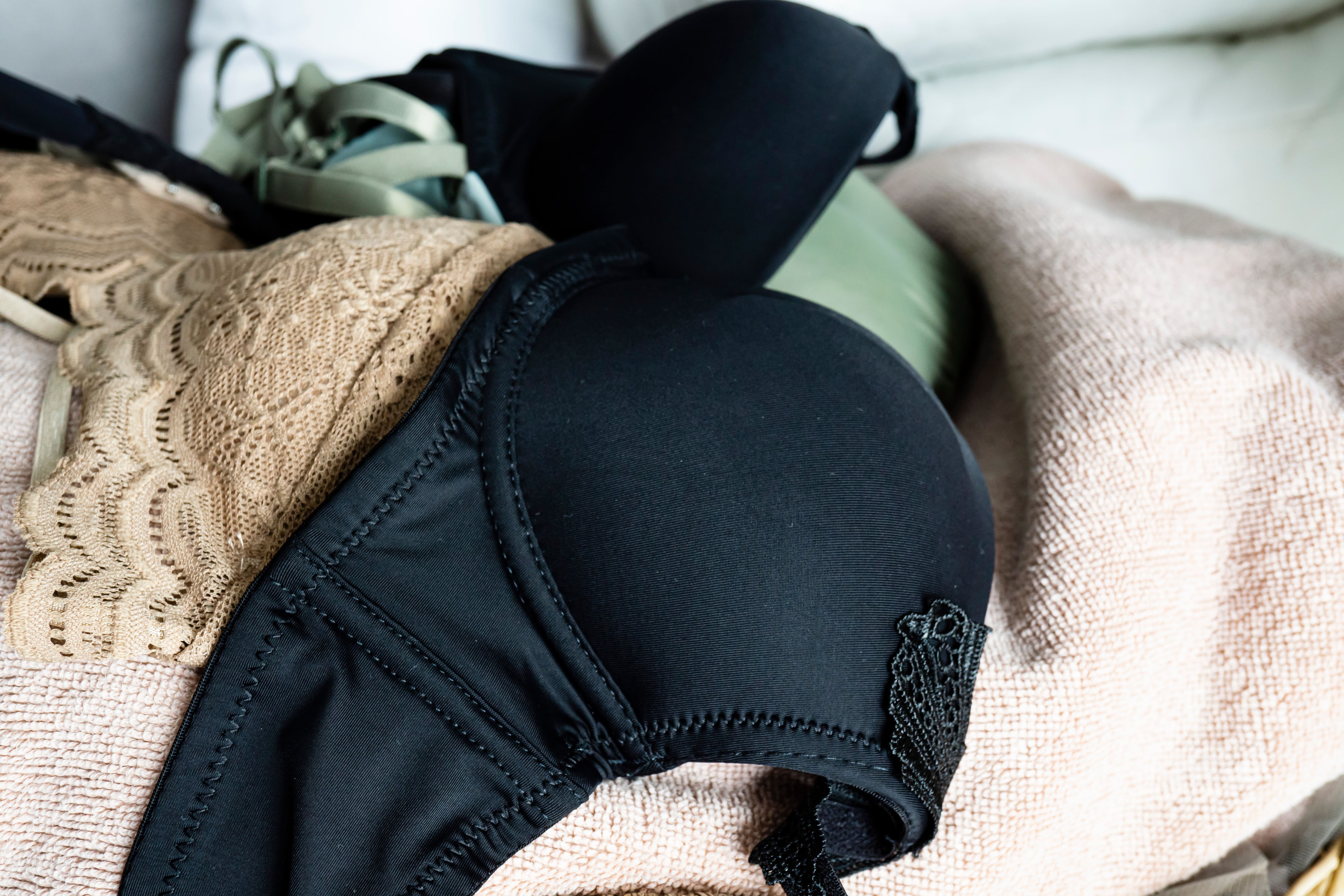 A nude bra, a black one, and a sage green bra piled up on a beige towel