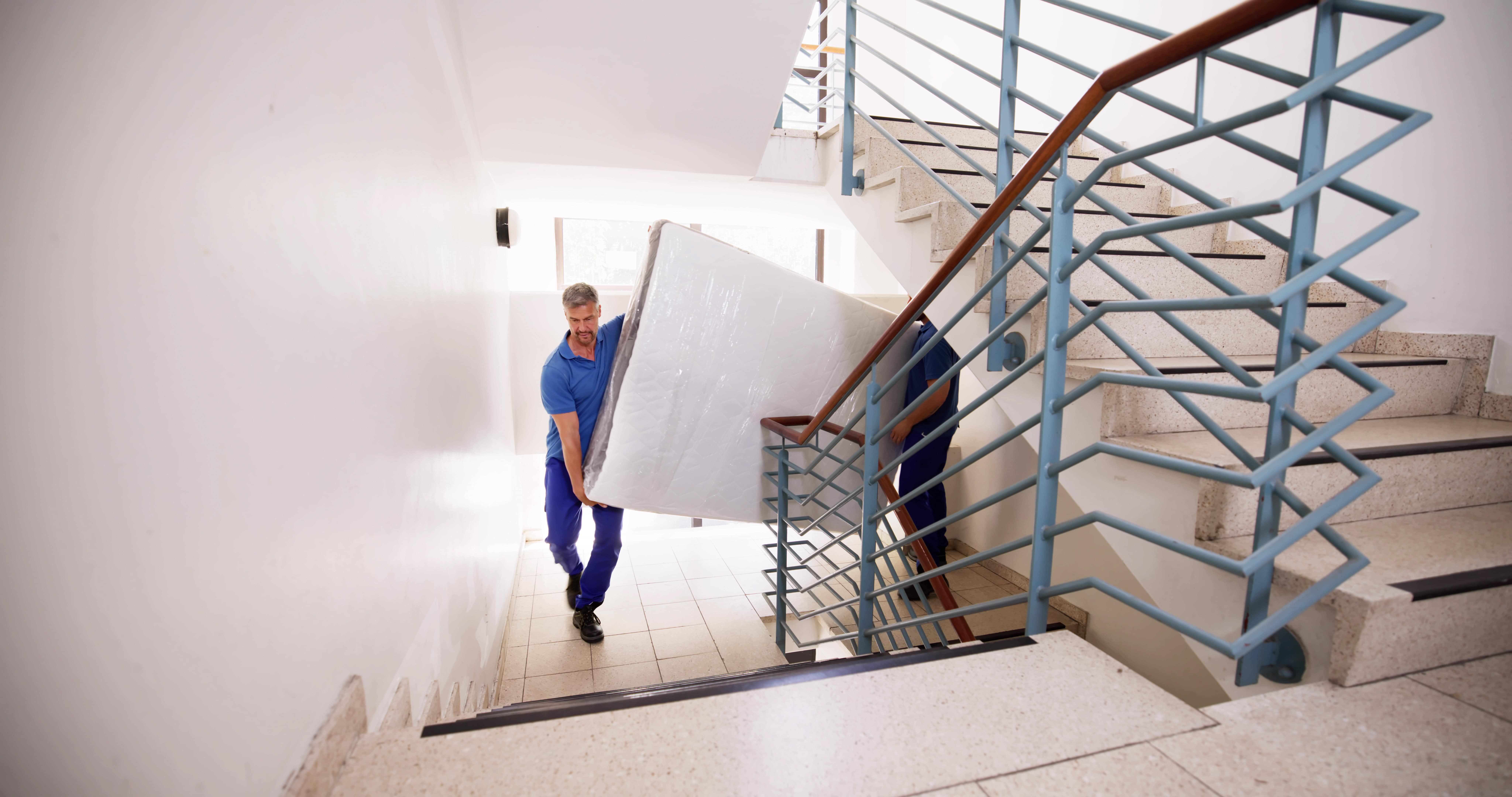 Two men carrying a mattress up a multi-storey staircase