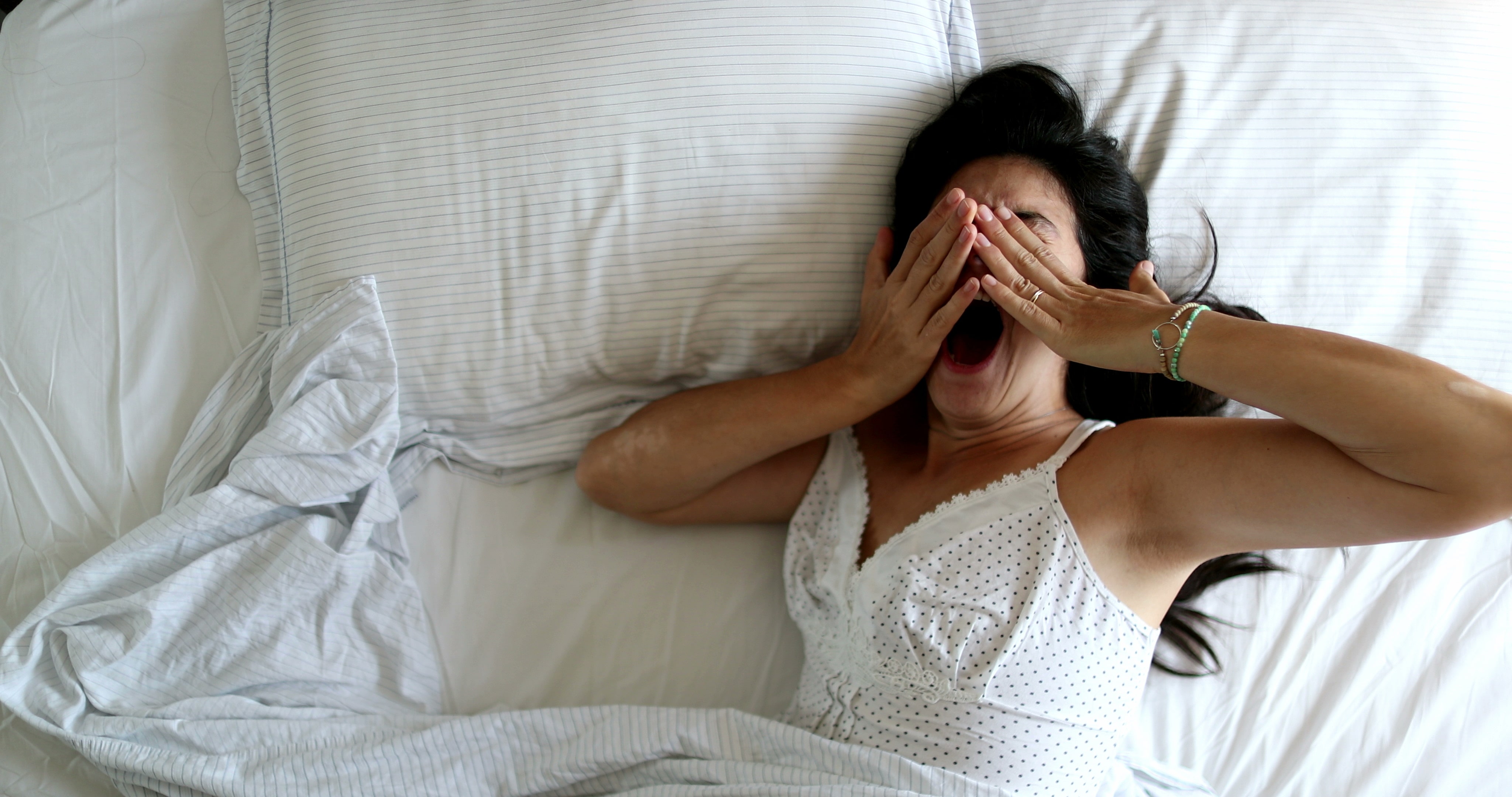 A woman yawning and stretching in her bed after having a poor night's sleep.