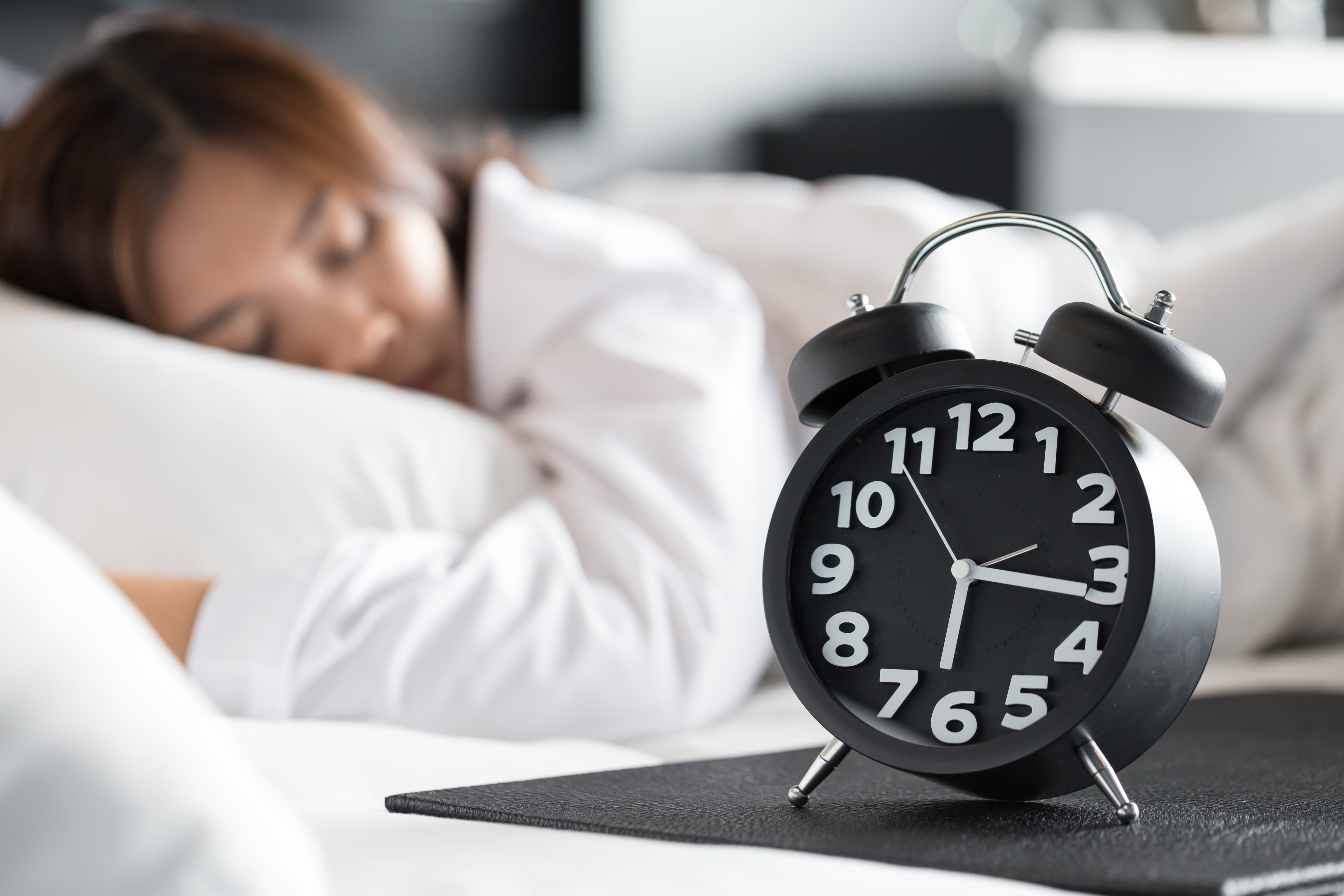 Alarm Clock in Foreground with Sleeping Woman in Bed in Background
