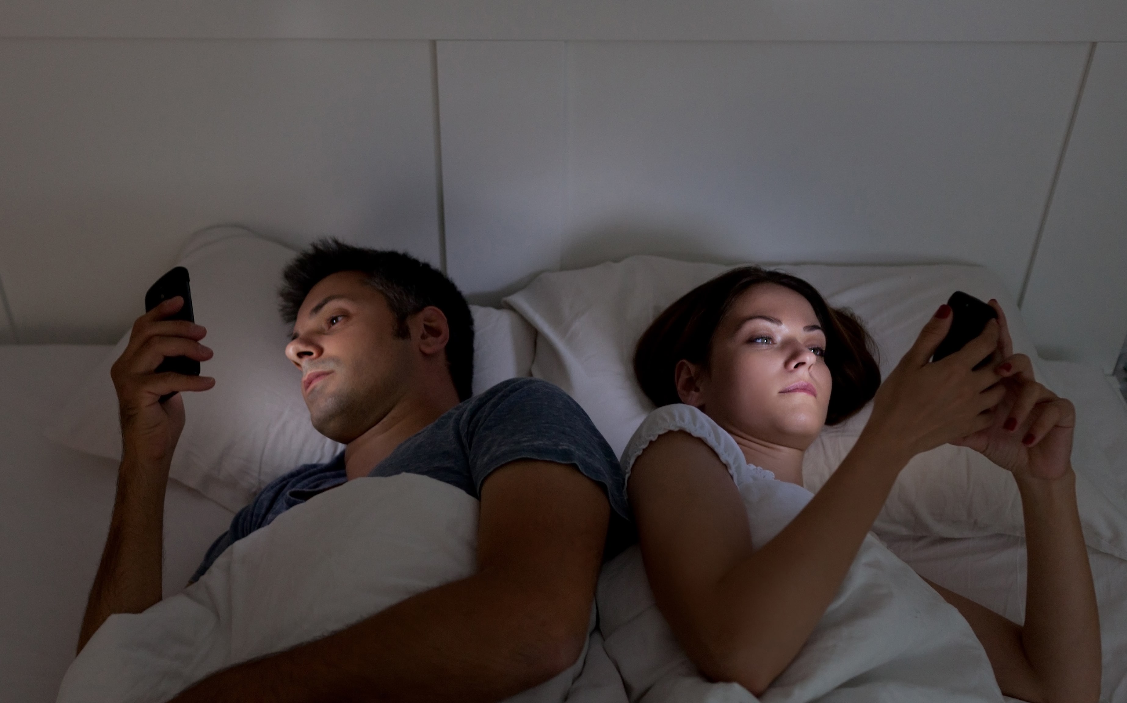 Couple in bed facing away from each other and looking at their mobile 'phones.