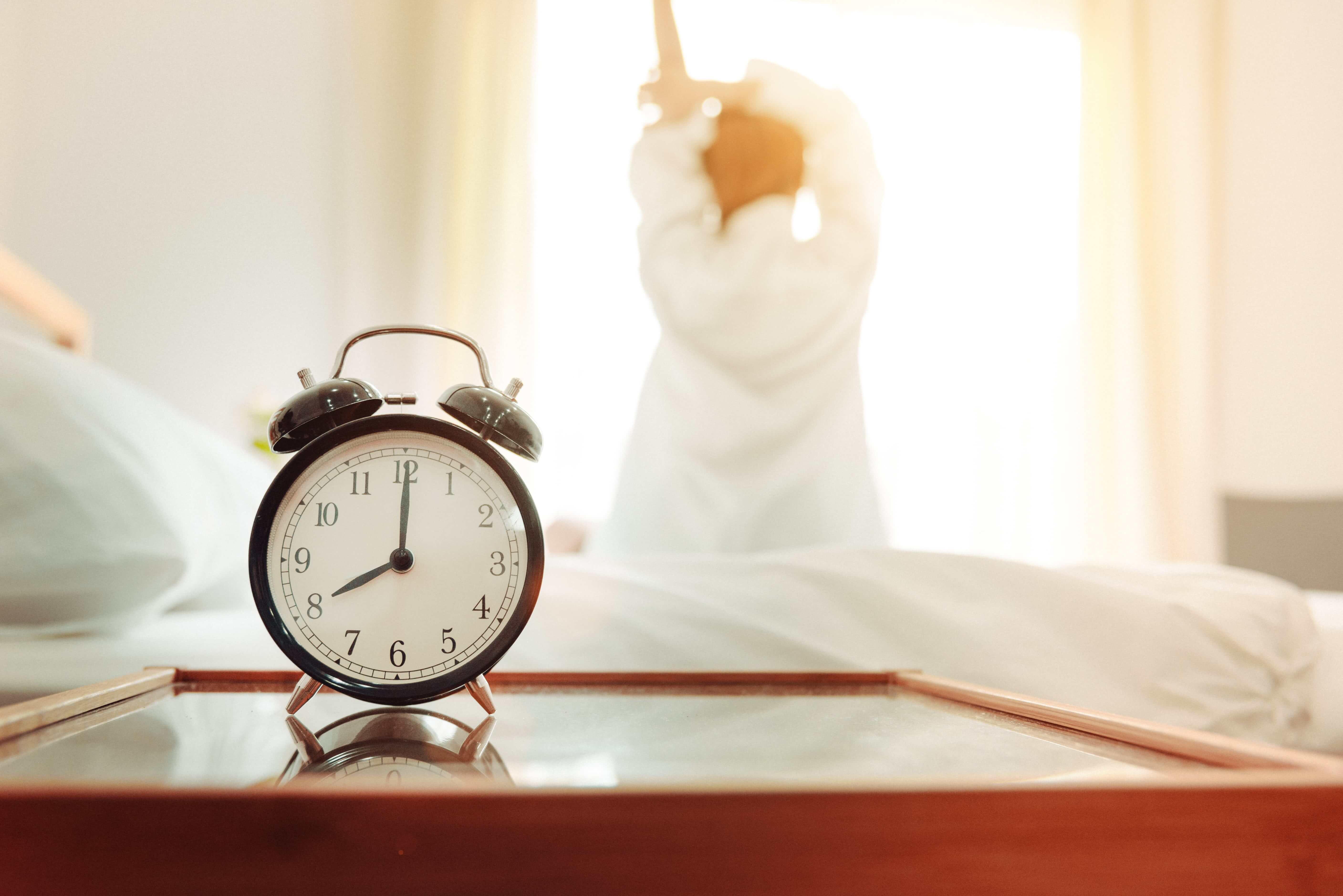 Alarm clock showing 8am with woman stretching after sleep