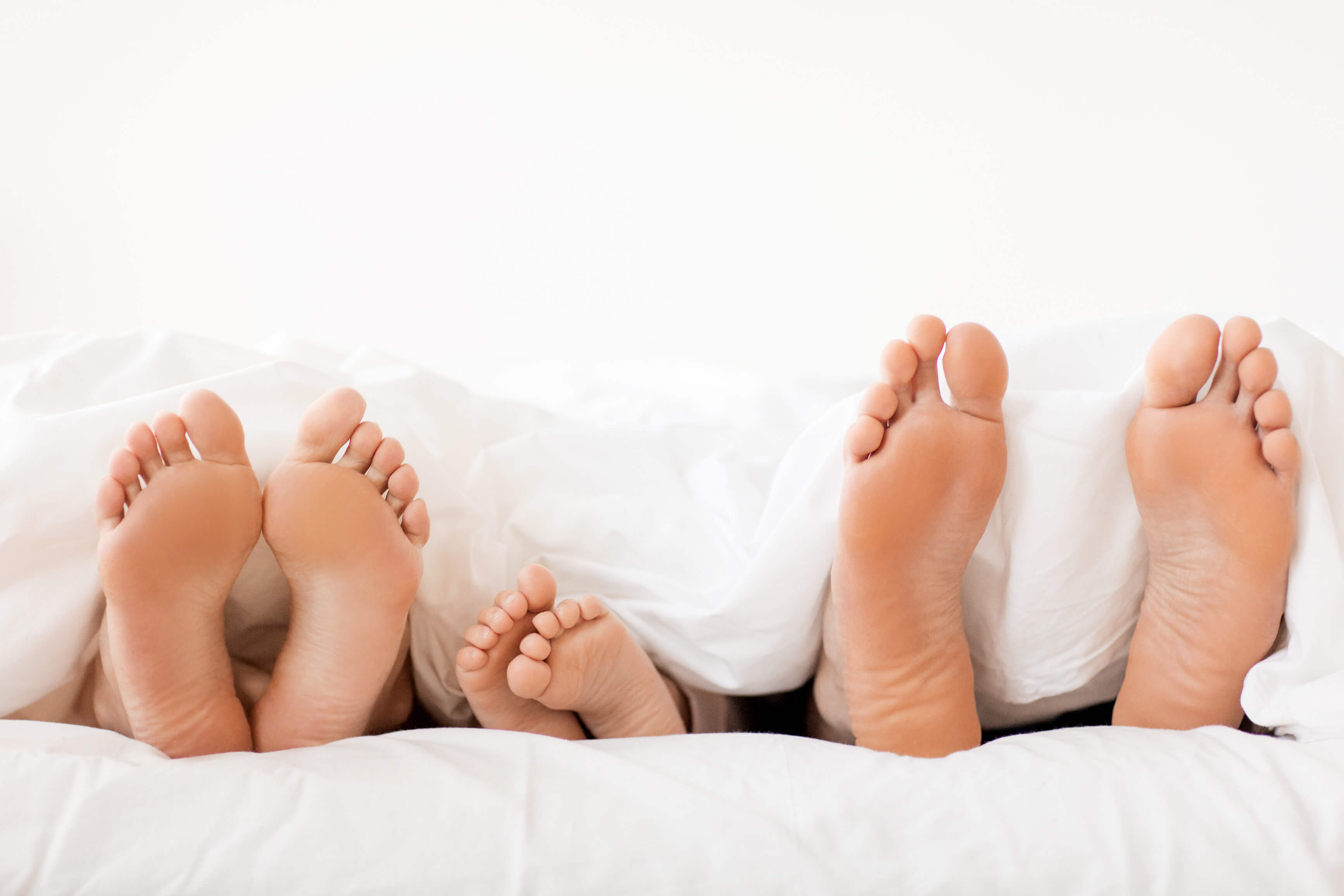 Bare soles of parents and their child in bed