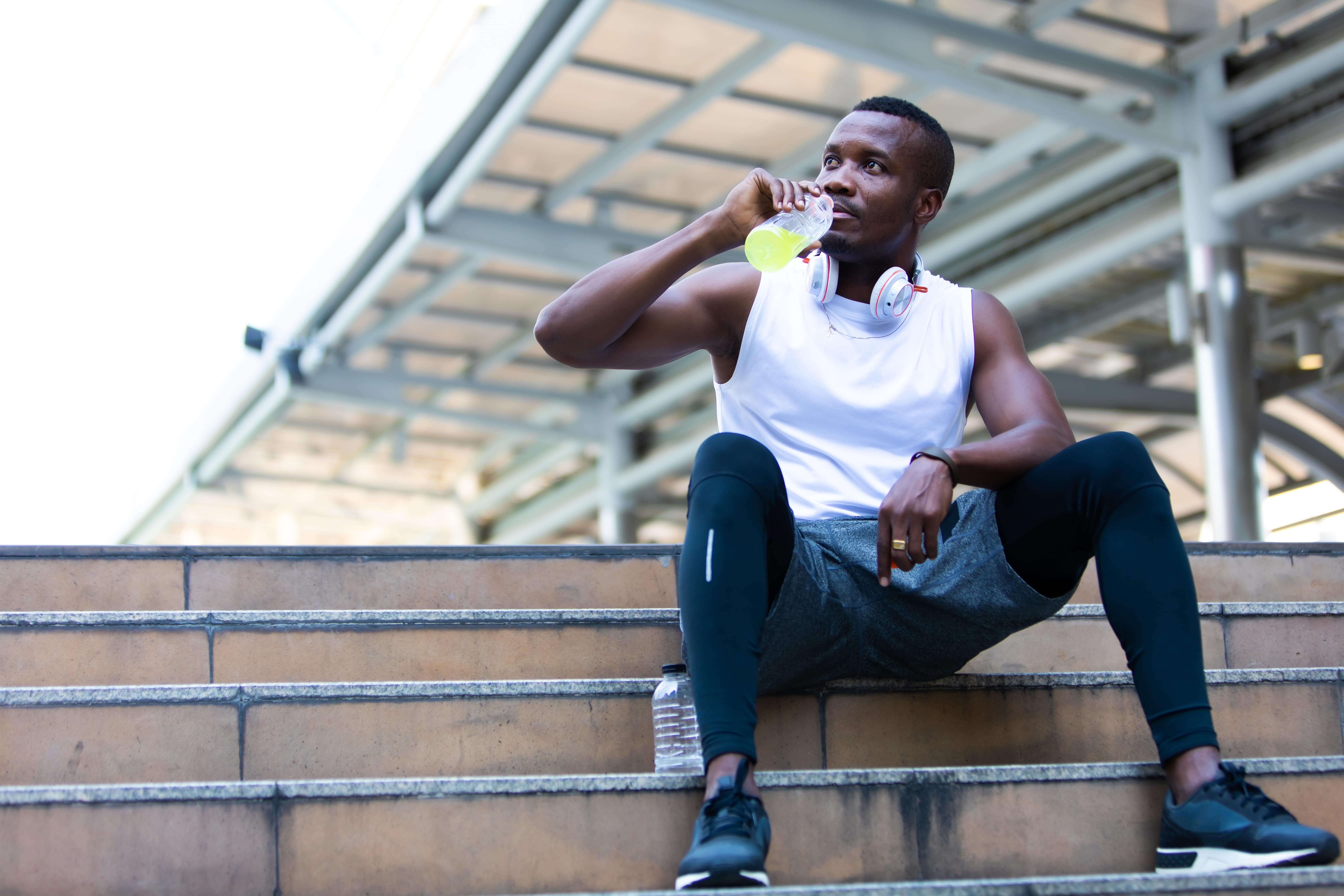 Black man sat on outdoor steps having a drink whilst taking an exercise break
