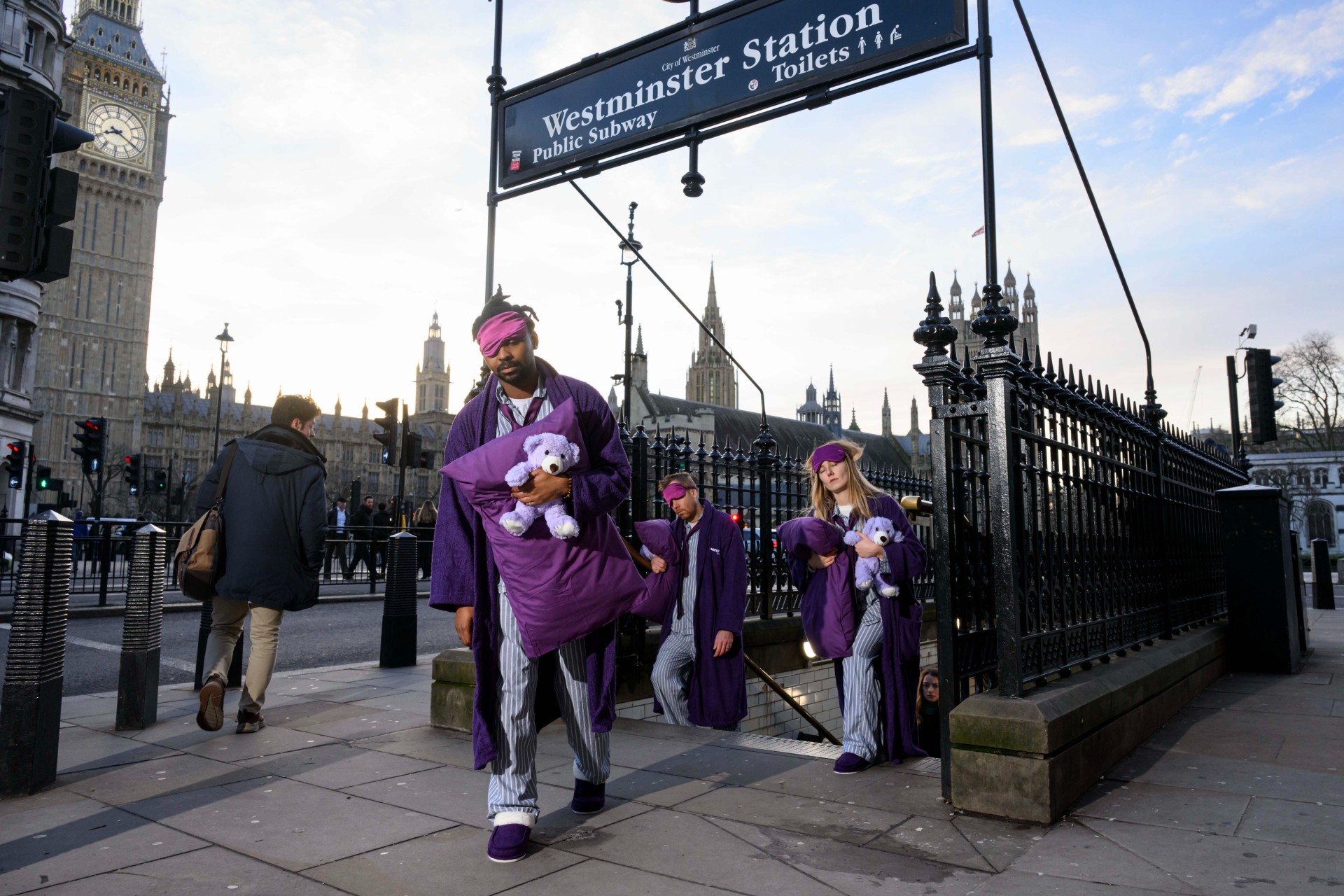 Three sleep deprived commuters emerging up the steps from Westminster Station wearing PJs, purple slippers, dressing gowns and sleep masks and carrying teddy bears