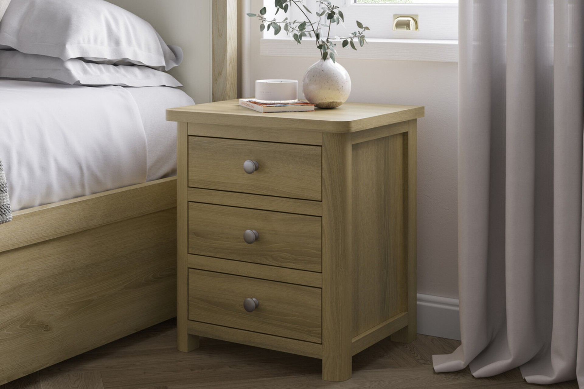 Delphine light oak 3 drawer bedside table with round silver handles pictured next to a matching oak bedframe