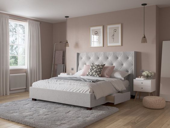 Romantic bedroom design ideas pinterest board with pink walls, pale grey upholstered bed frame, a fluffy rug and pouf, and some white roses on the bedside table.