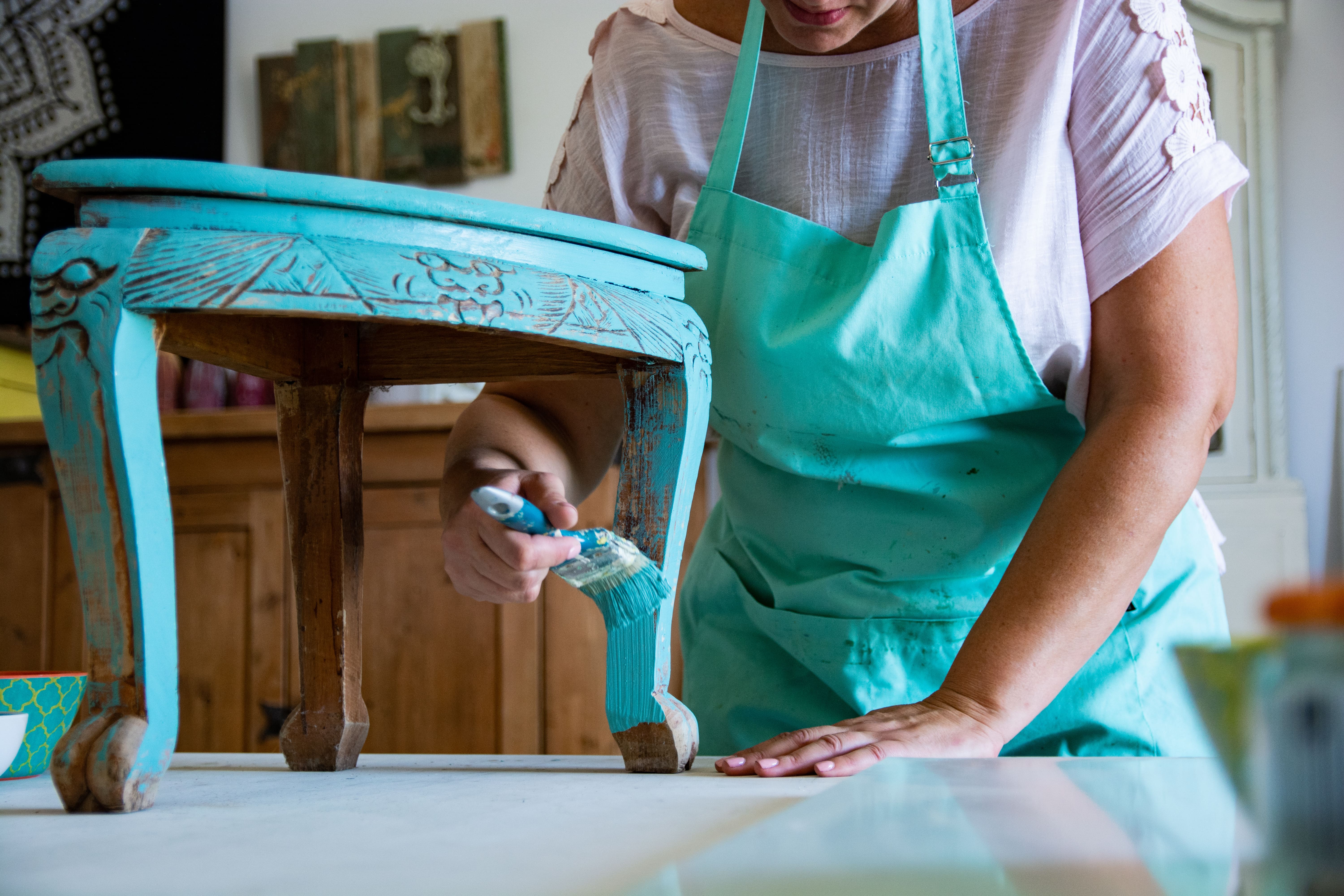 A lady upcycling a decorative wooden stool by painting it teal